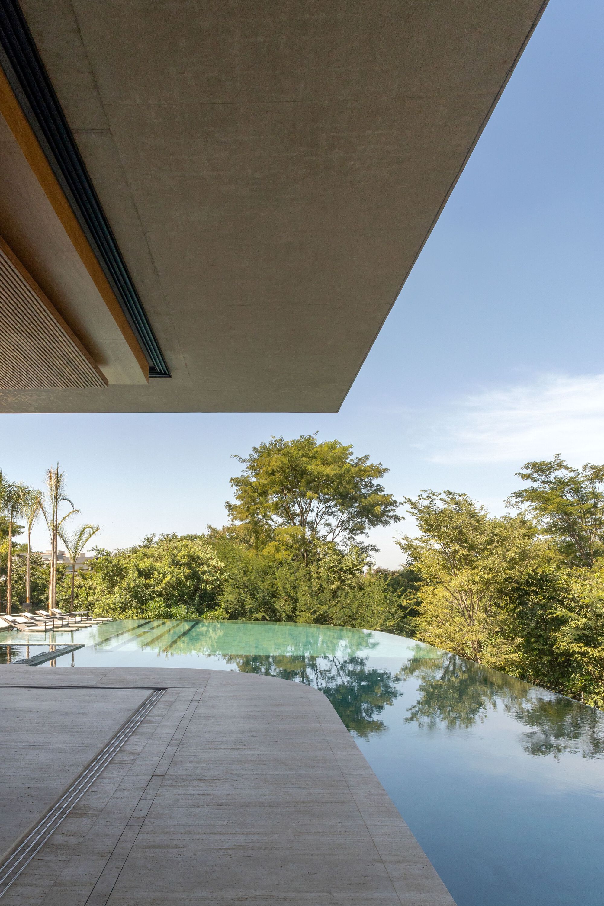 Infinity pool edge reflecting the surrounding trees beneath a concrete canopy soffit
