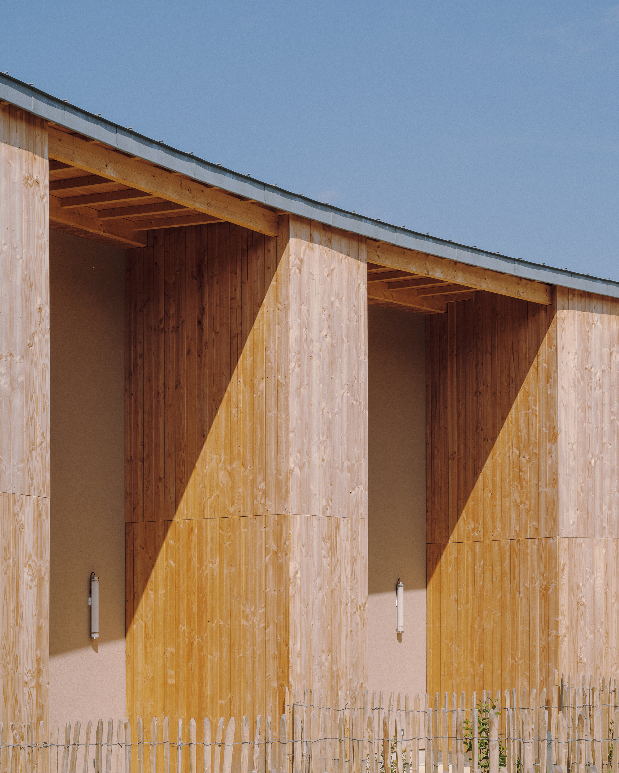Close-up of timber facade panels with exposed rafters creating triangular shadow patterns in afternoon light