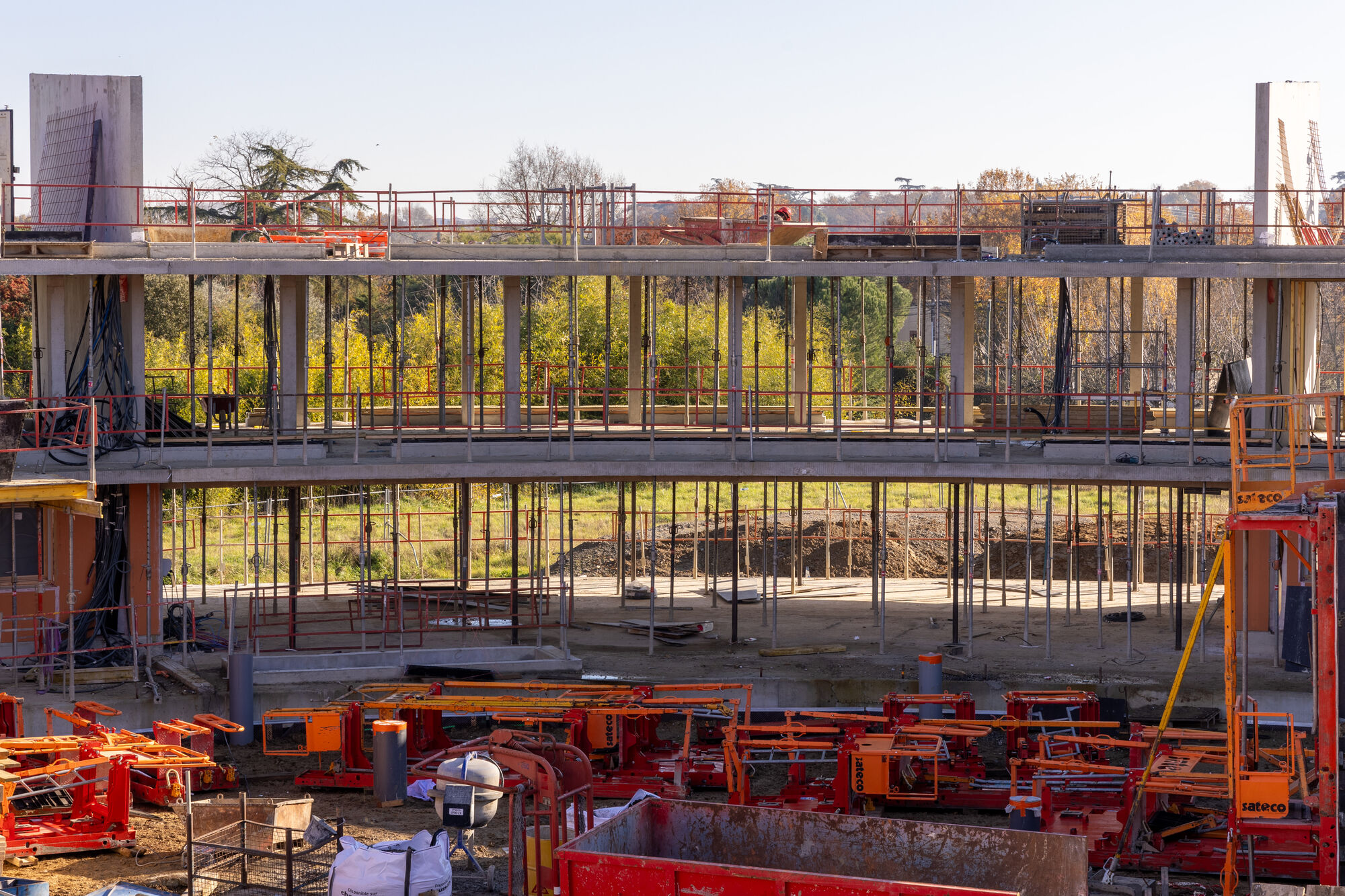 Construction view of the concrete floor slabs and steel columns with scaffolding and autumn trees beyond