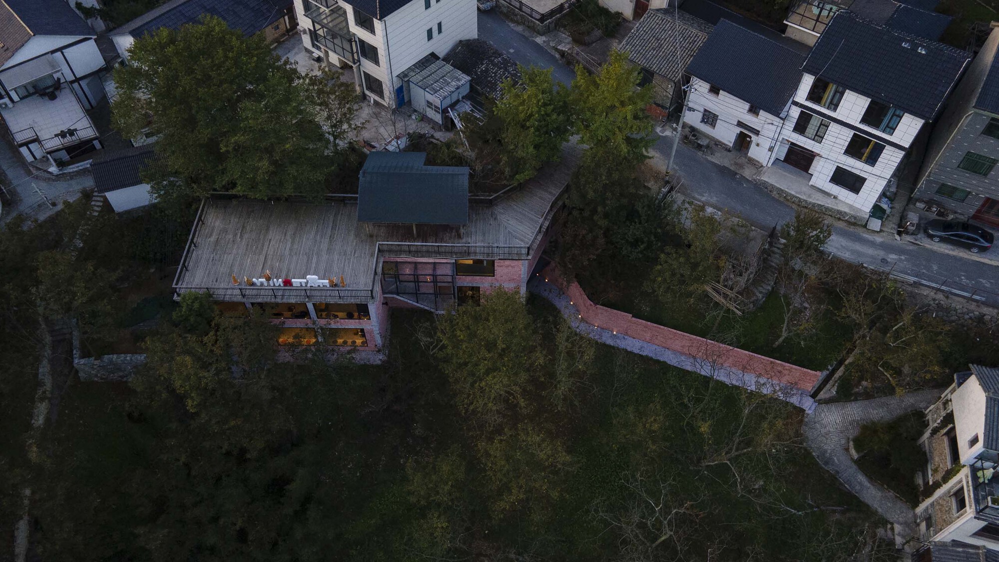 Aerial view of the timber deck roof and curved rammed earth wall amid dense tree cover