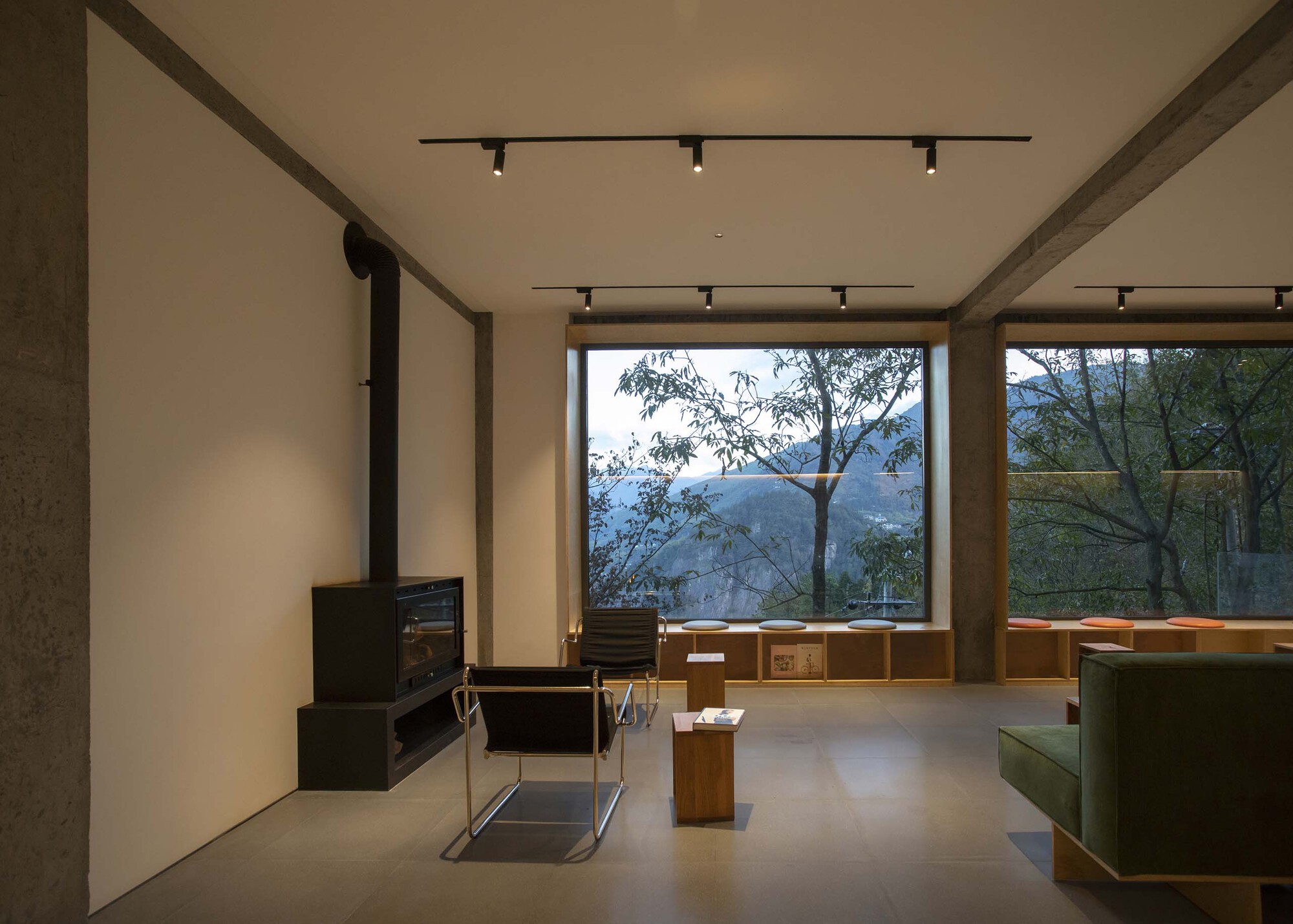Interior lounge with exposed concrete beams, wood-framed window overlooking misty mountains, and black track lighting