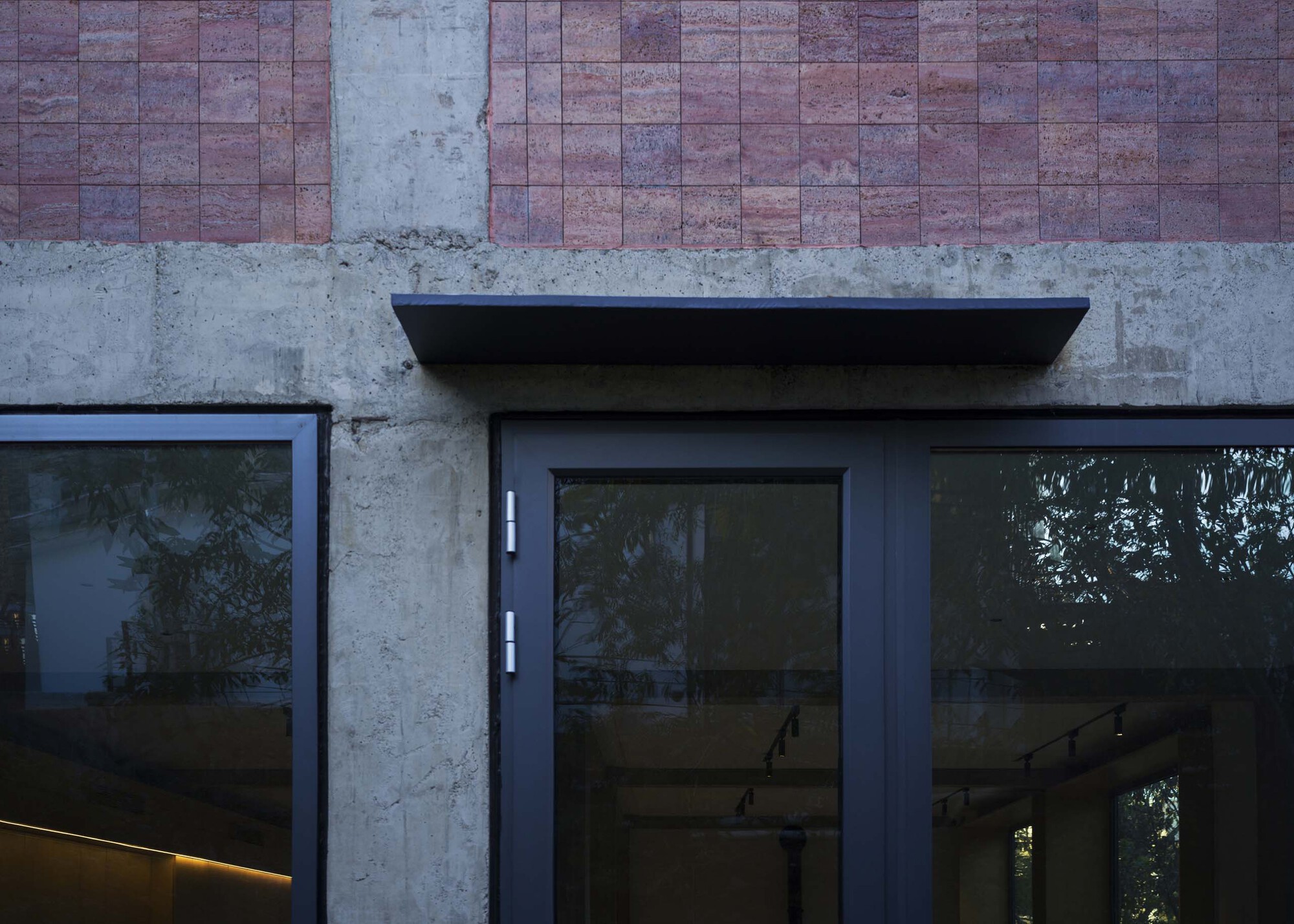 Black steel canopy over glass door set into concrete and rammed earth tile facade