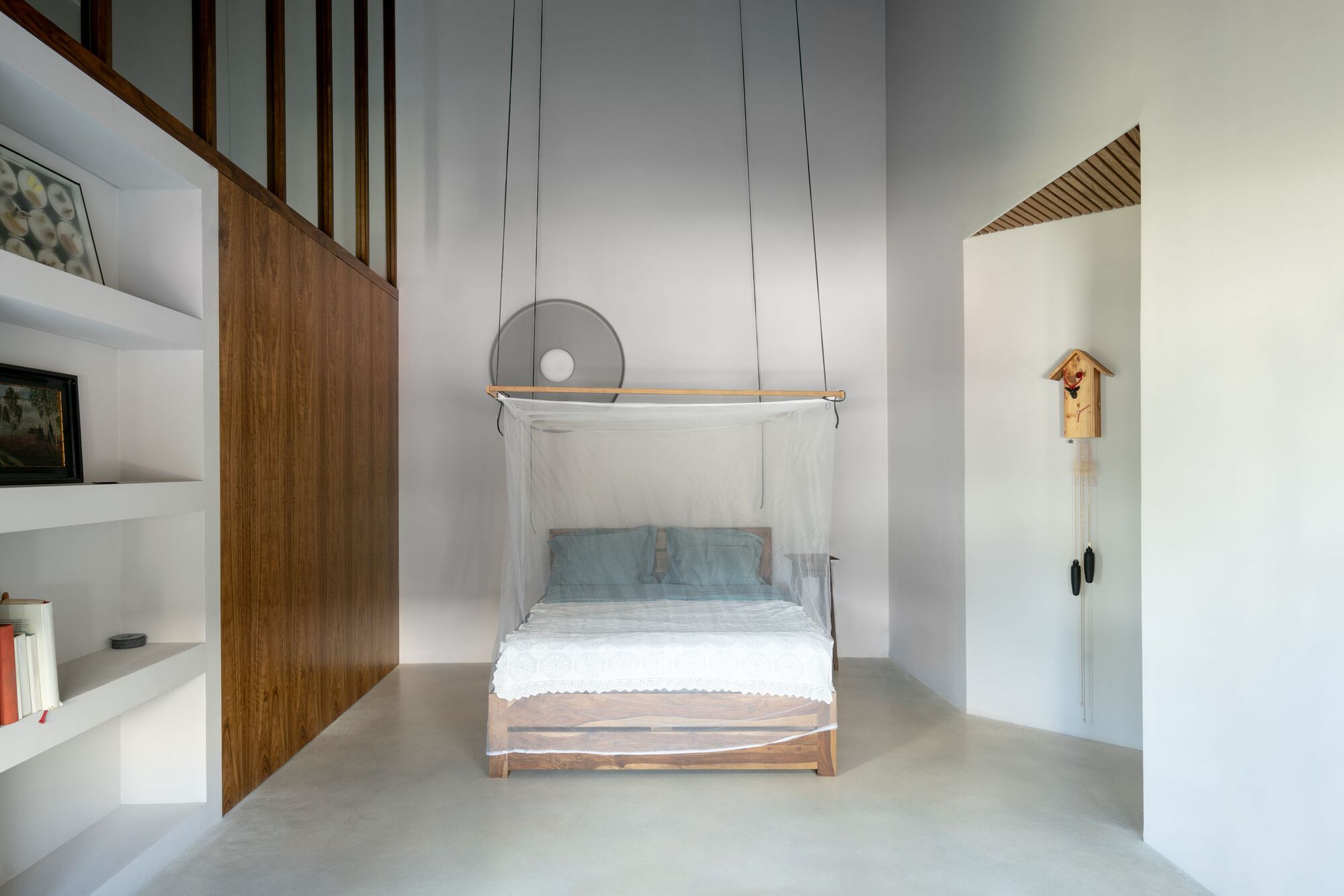 Bedroom with suspended timber bed frame and mosquito netting beneath vertical wood slats and high ceiling