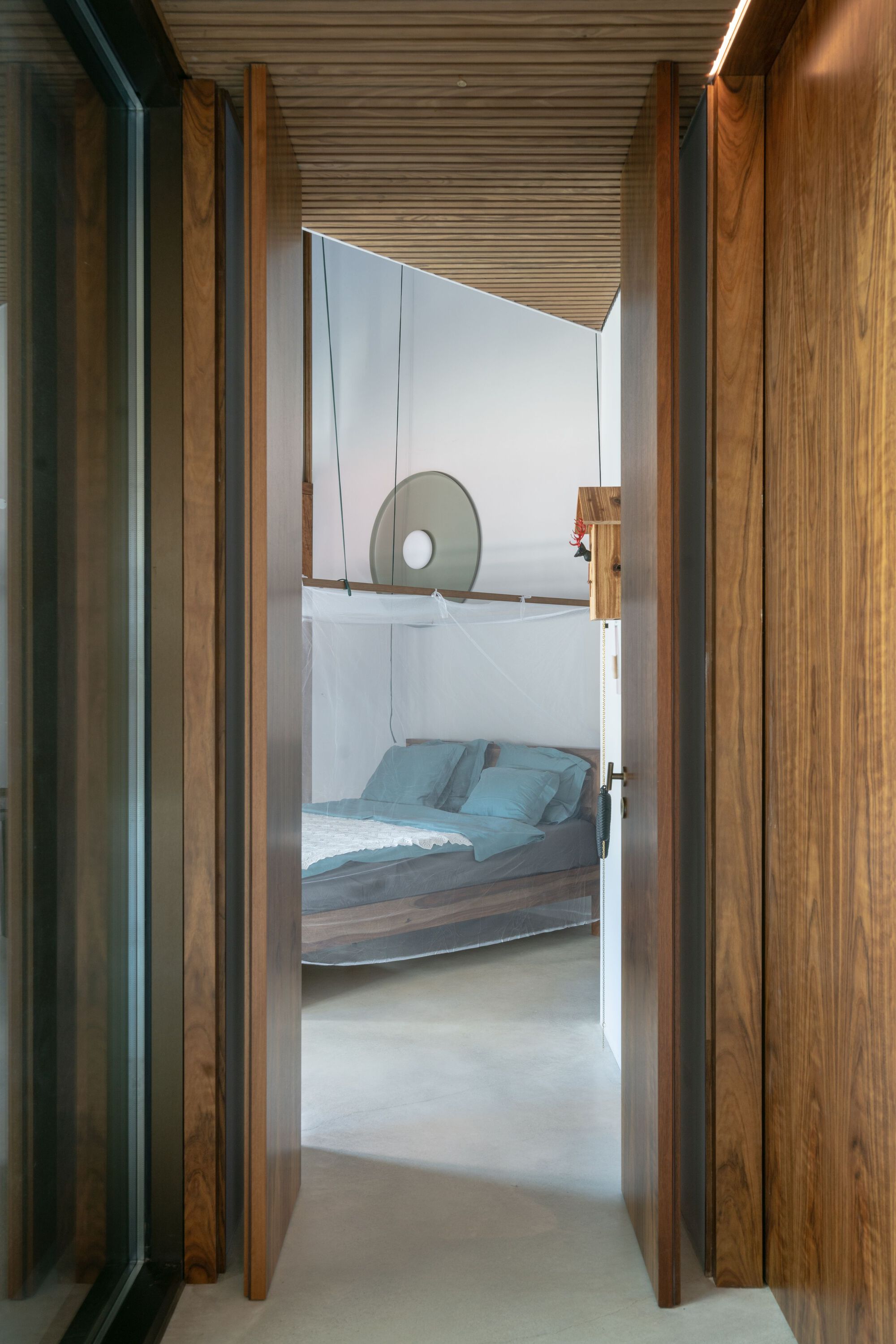 View through timber doorway into bedroom with slatted wood ceiling and suspended canopy bed