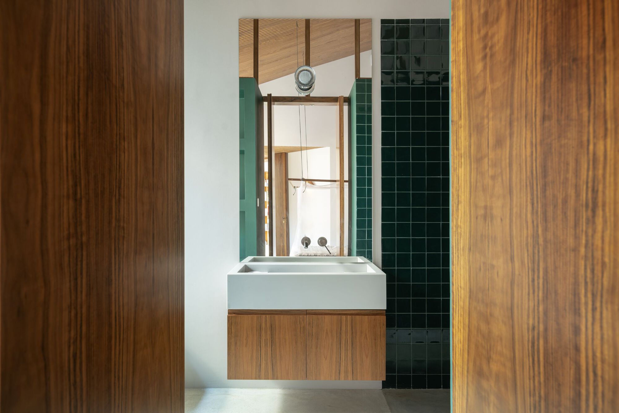 Bathroom vanity with timber cabinetry framed by wood panels and dark green tiled shower beyond