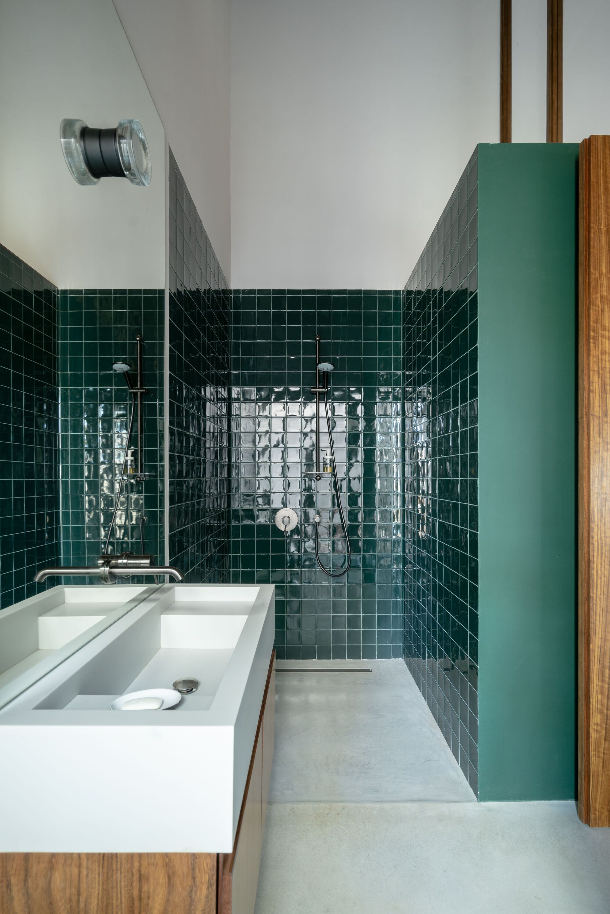 Bathroom with glossy dark green square tiles, white sink, and green painted partition beside timber cladding
