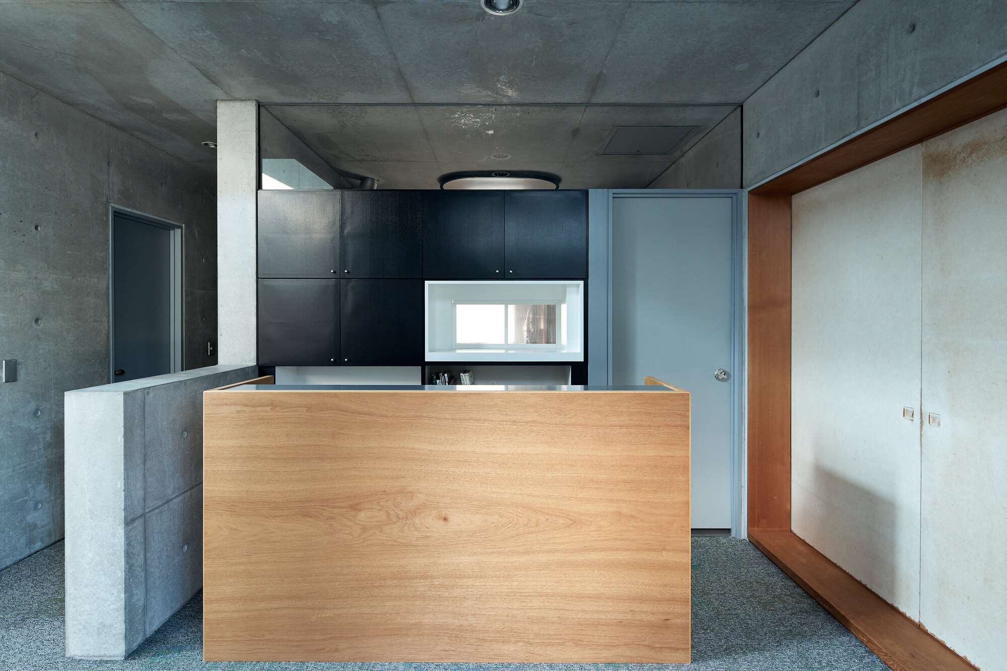 Kitchen with timber island and black cabinetry beneath exposed concrete ceiling and structural column