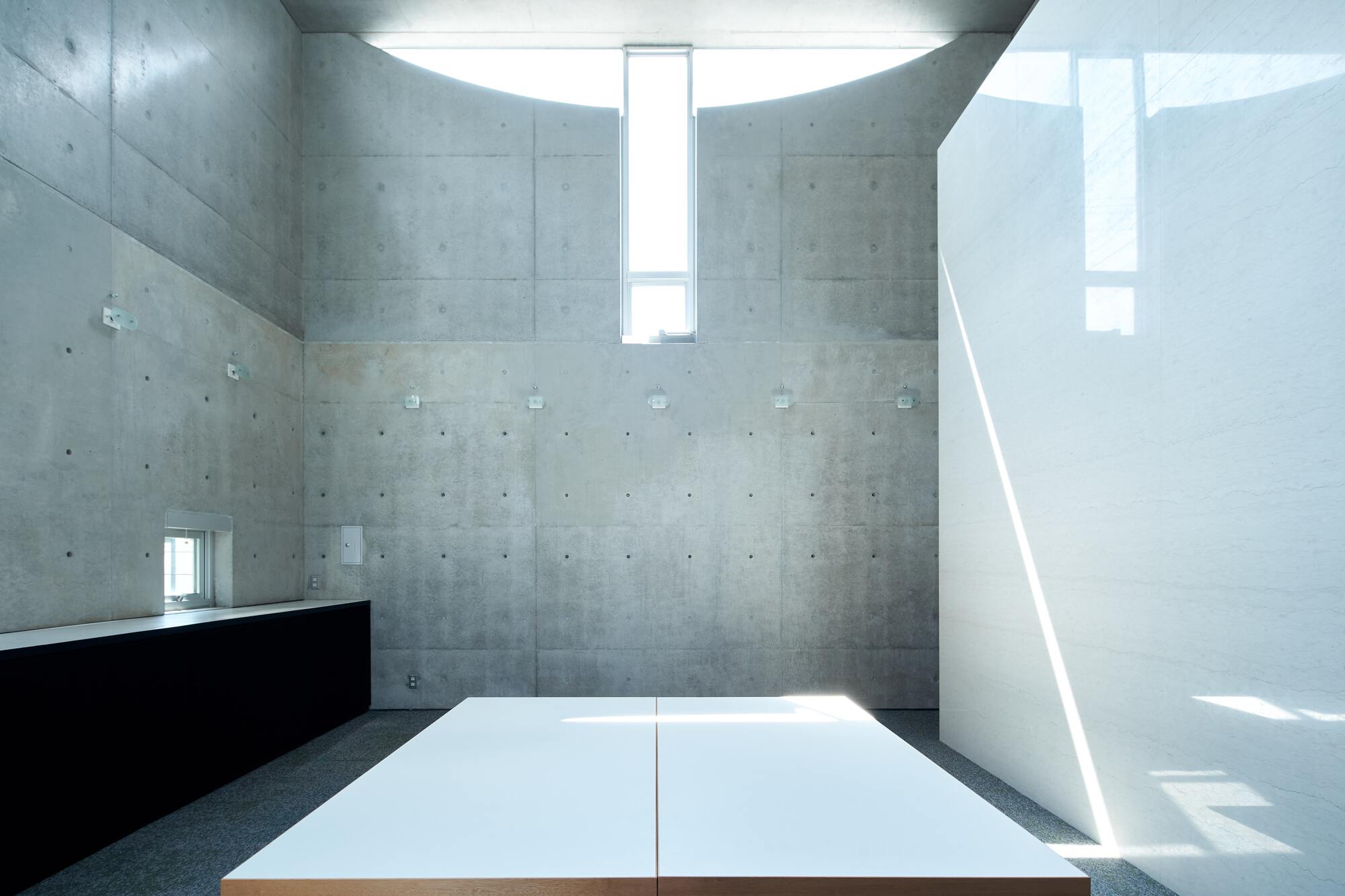 Double-height concrete interior space with vertical skylight and white platform flooring in bright daylight