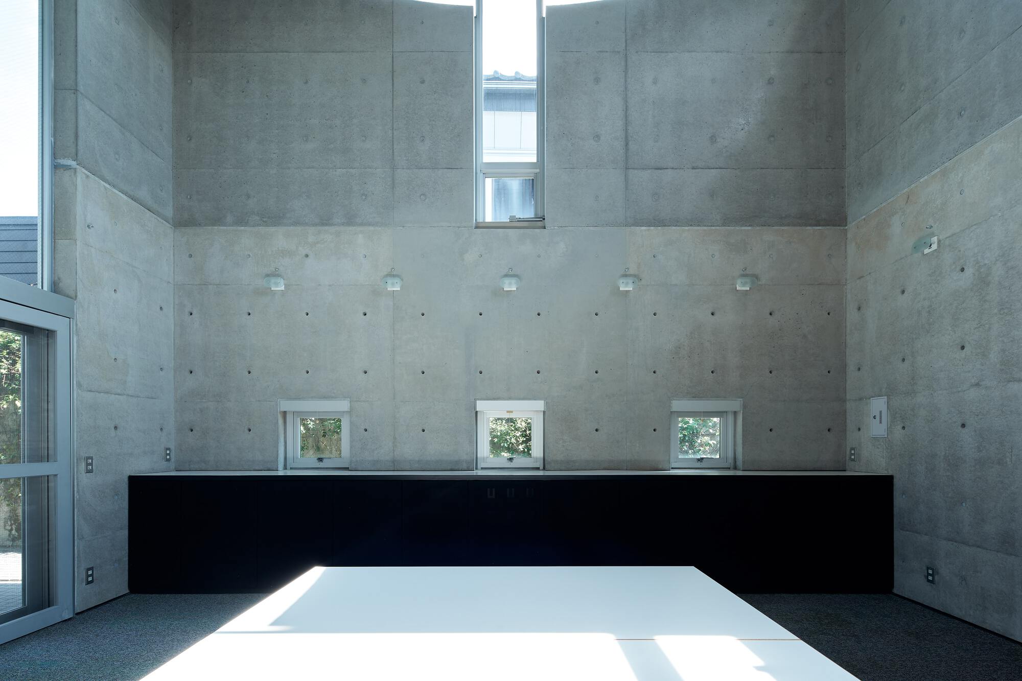 Concrete walls with small punched windows and a black horizontal band above the white floor