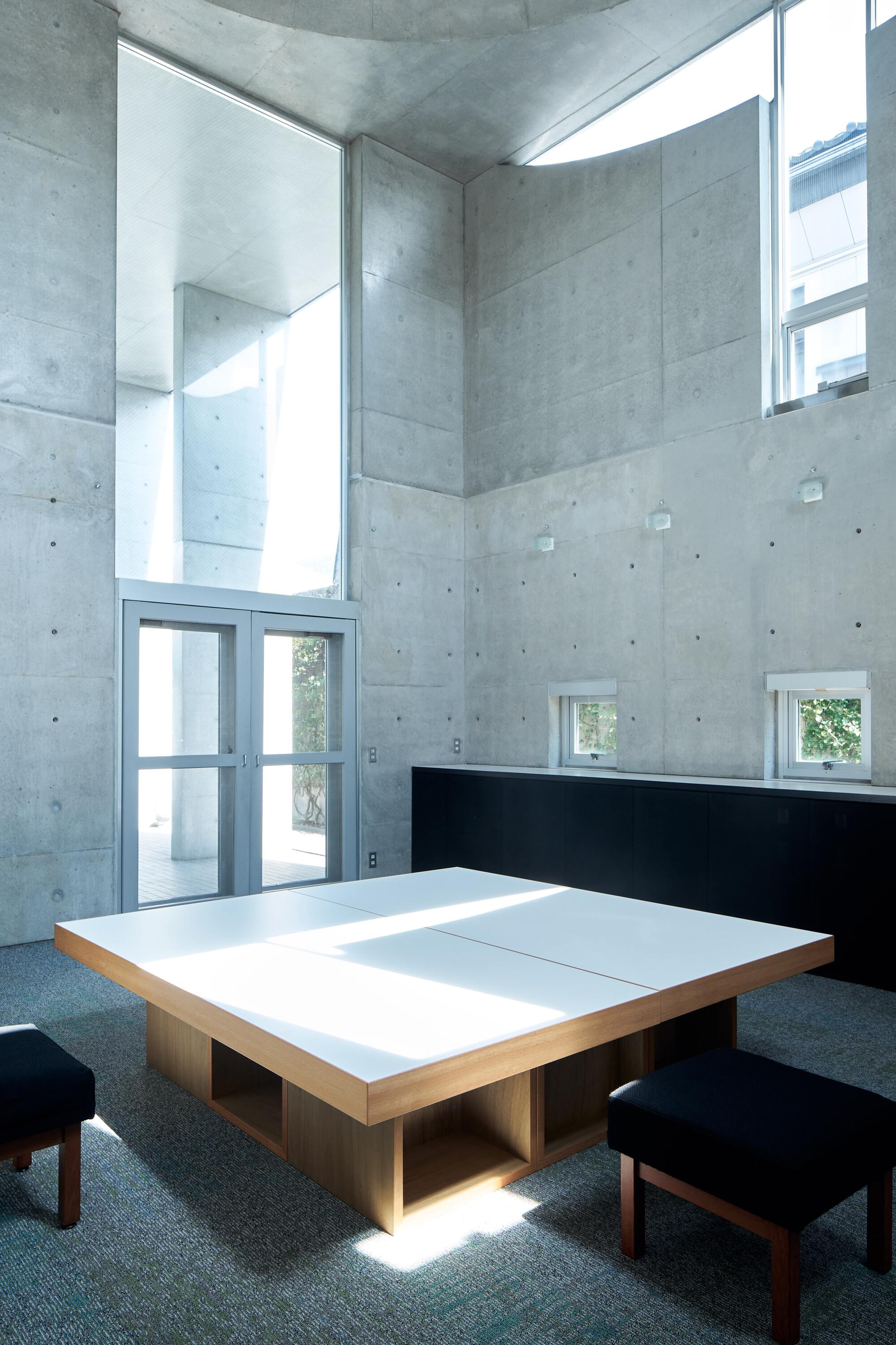 Low wooden table with white top surface beneath a tall concrete ceiling with clerestory glazing