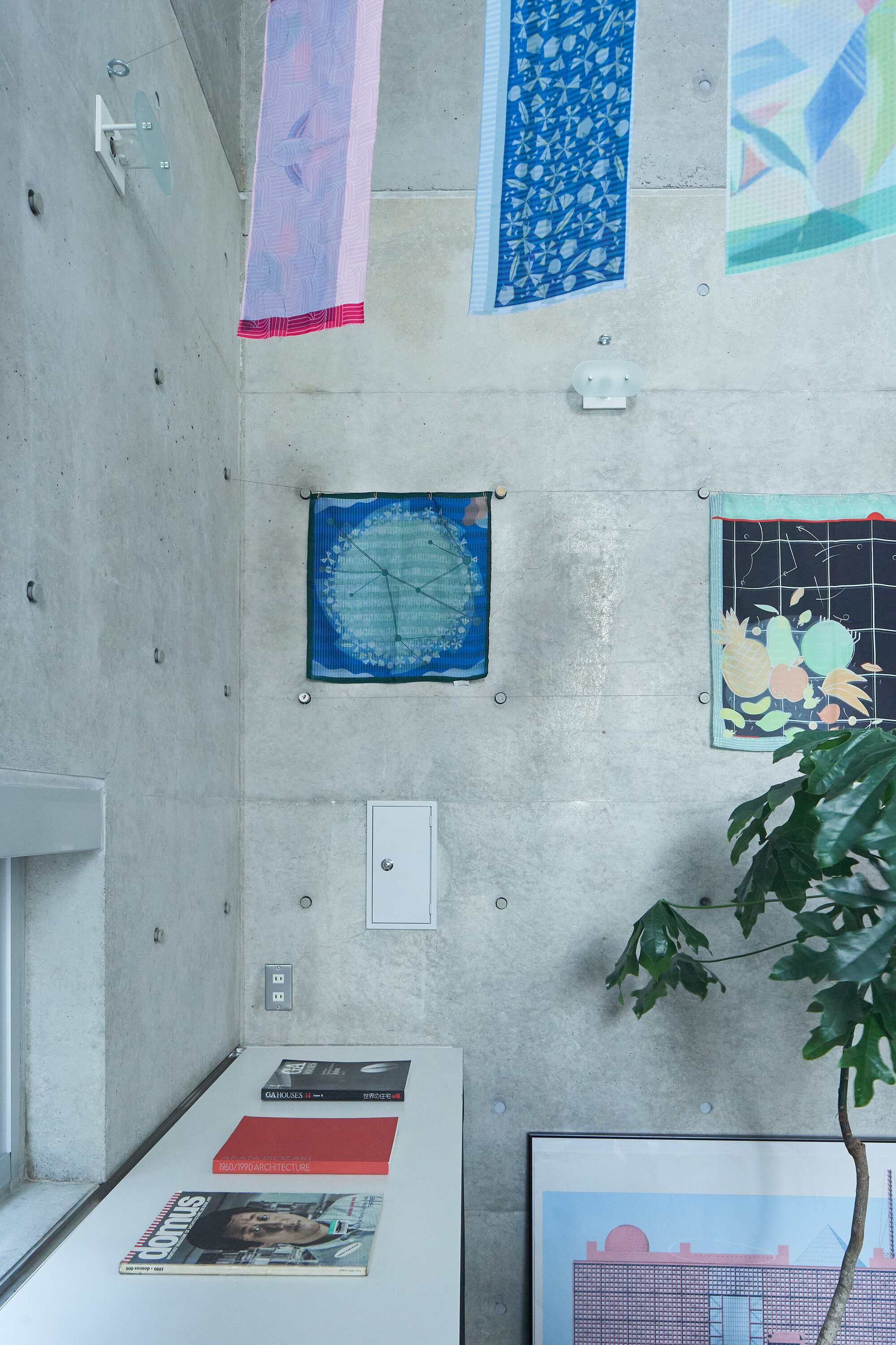 Overhead view of a white work surface with patterned fabric panels pinned to the concrete wall and a potted plant
