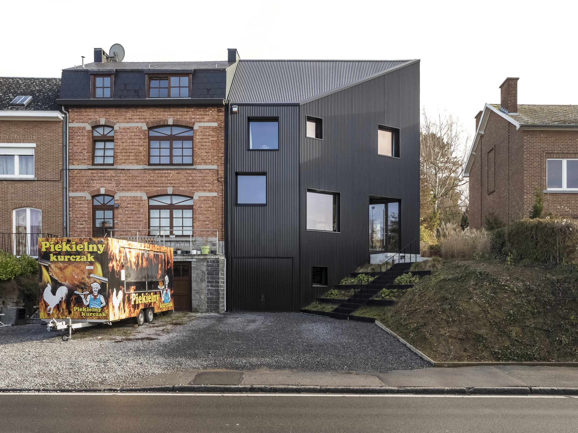 Street view of the black corrugated metal facade nestled between brick buildings with a food truck parked in front