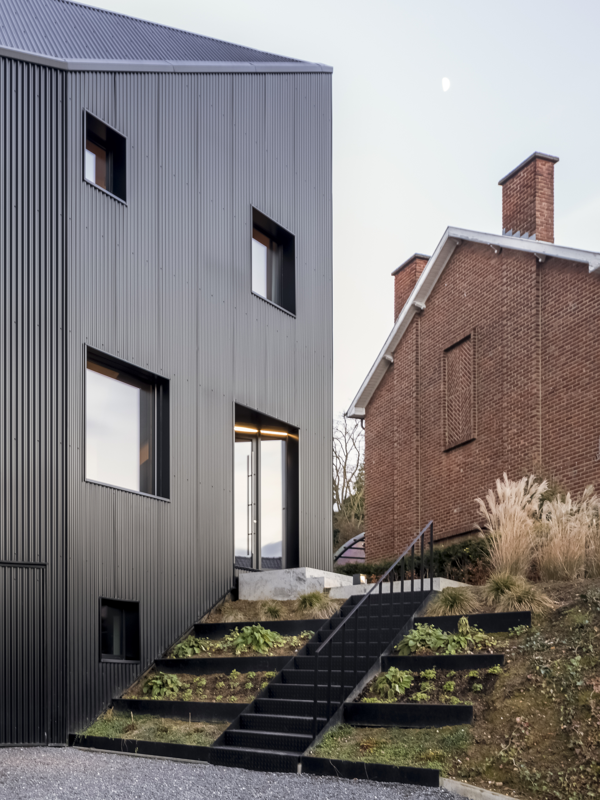 Exterior view showing the terraced planted beds ascending black steel stairs toward the rear entrance