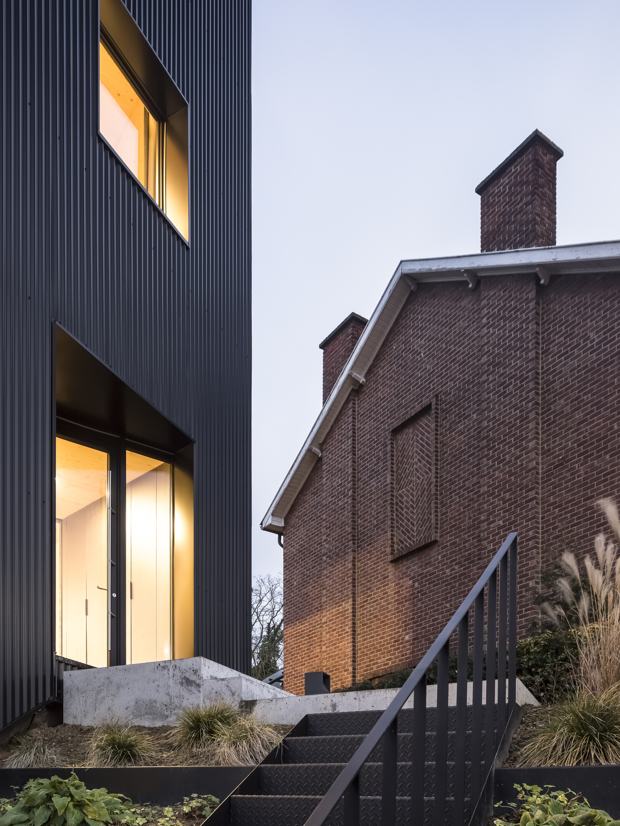 Close-up of the illuminated windows and concrete threshold at dusk beside the ornamental grasses