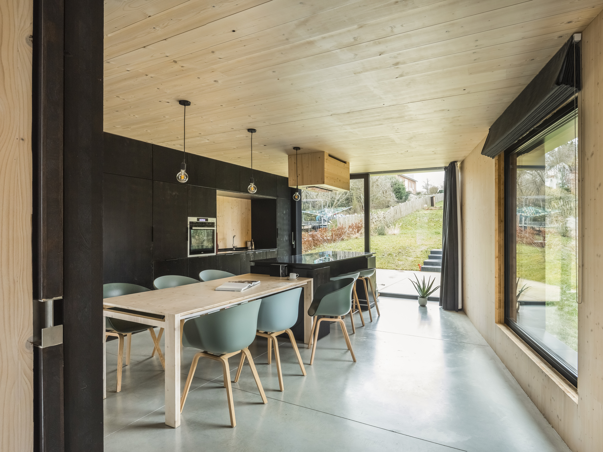 Open-plan dining area with pale timber ceiling, black cabinetry, and floor-to-ceiling glazing to the garden
