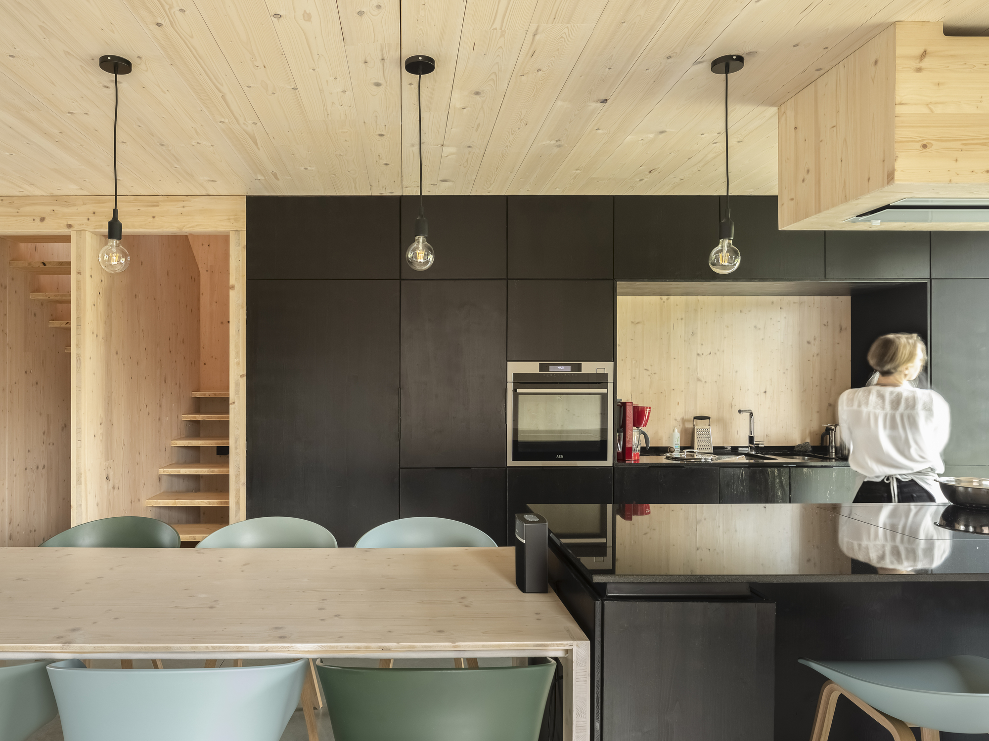 Kitchen with dark steel cabinets and timber panels flanked by a visible timber staircase beyond