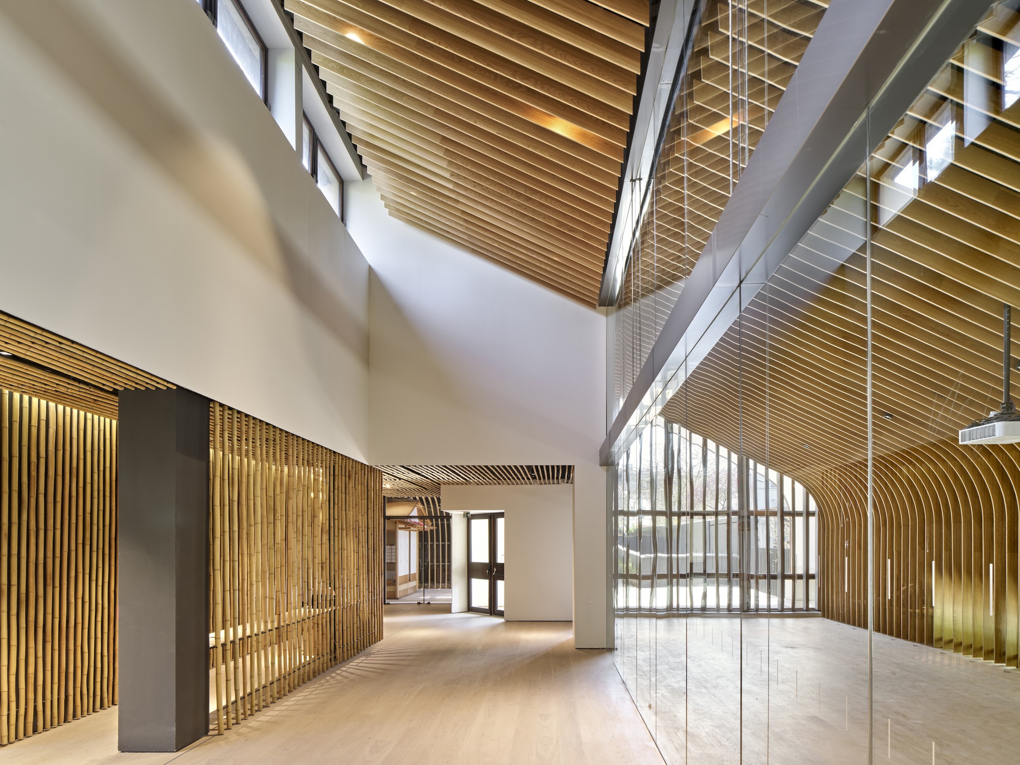 Double-height lobby with timber slatted ceiling and glass-walled mezzanine level above pale wood flooring