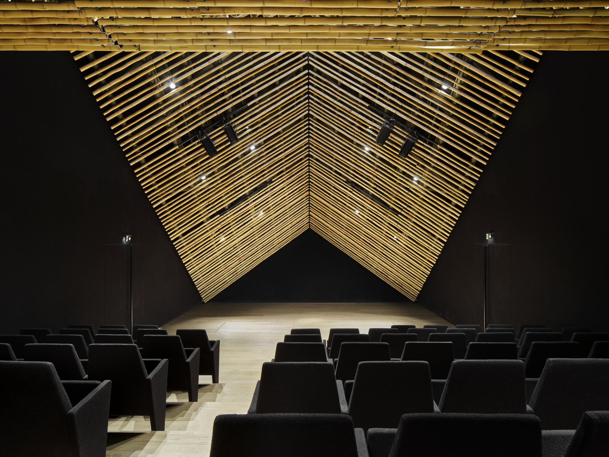 Front view of the auditorium stage with folded timber baffle ceiling forming a geometric chevron pattern