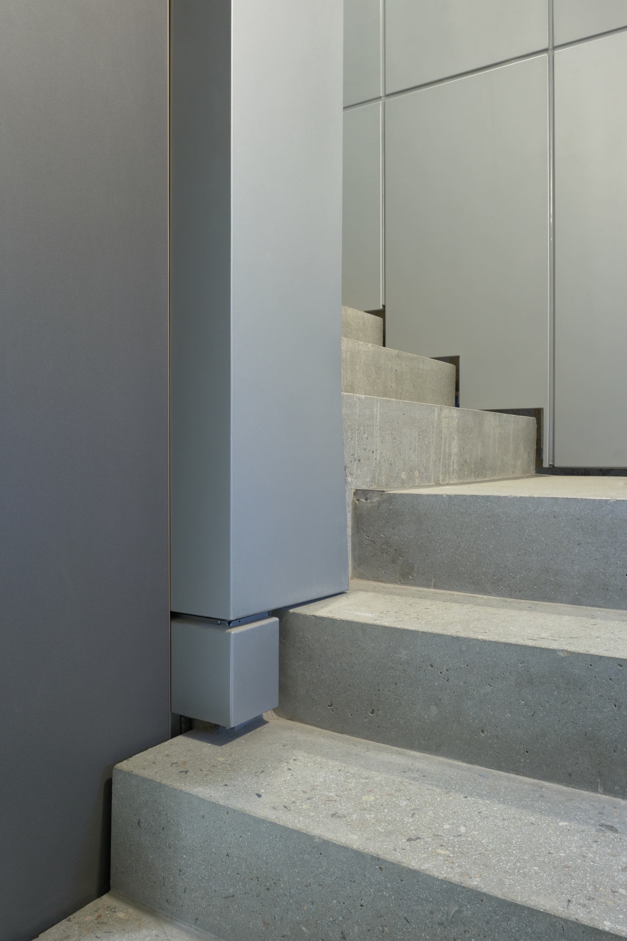 Concrete stair treads meeting grey metal wall panels and vertical column in natural light