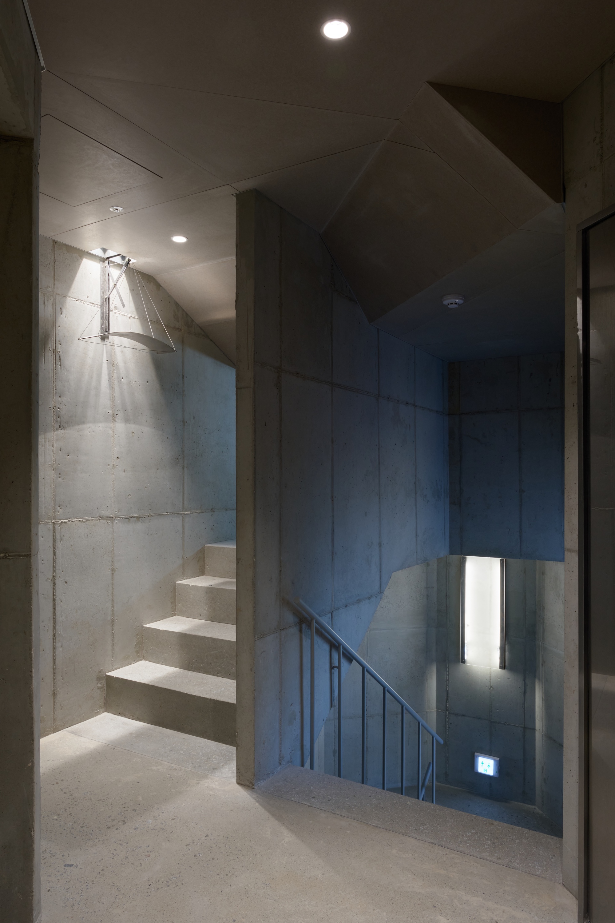Concrete stairwell with floating treads, metal handrail and narrow vertical window illuminating the landing