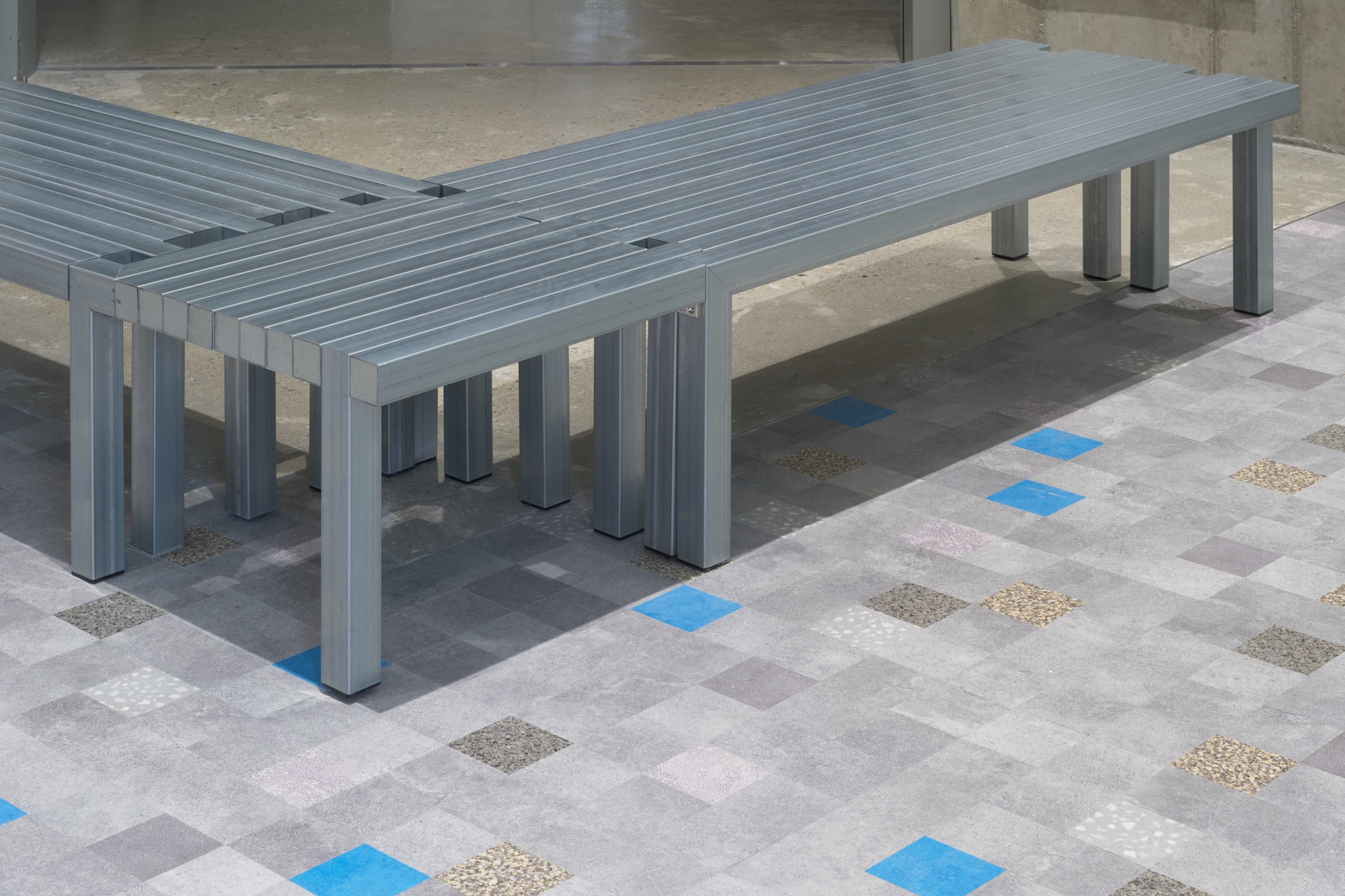 Grey slatted benches on multicolored terrazzo tile floor with blue and beige inlays