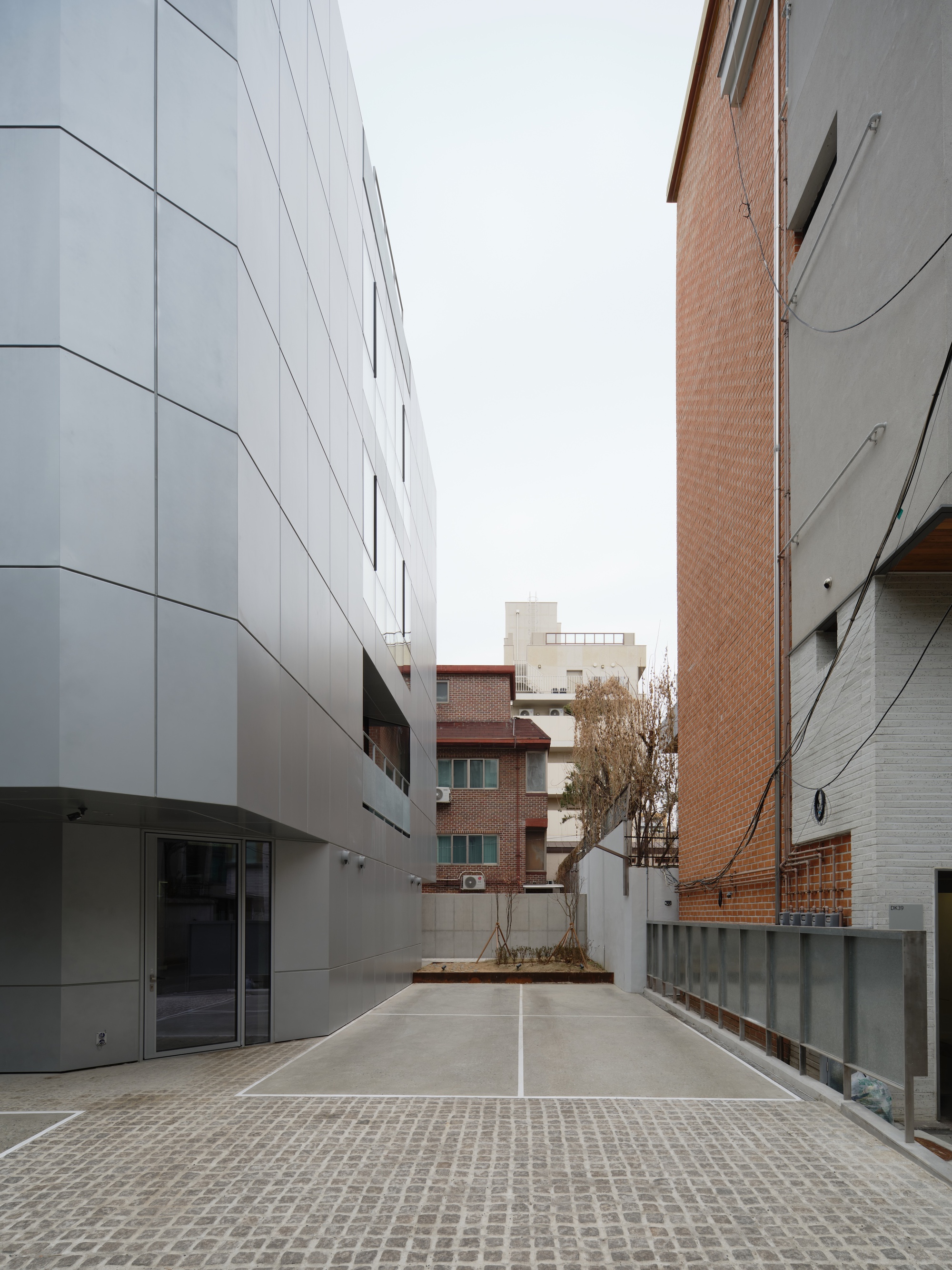 Narrow alley between white paneled facade and brick buildings with bare tree