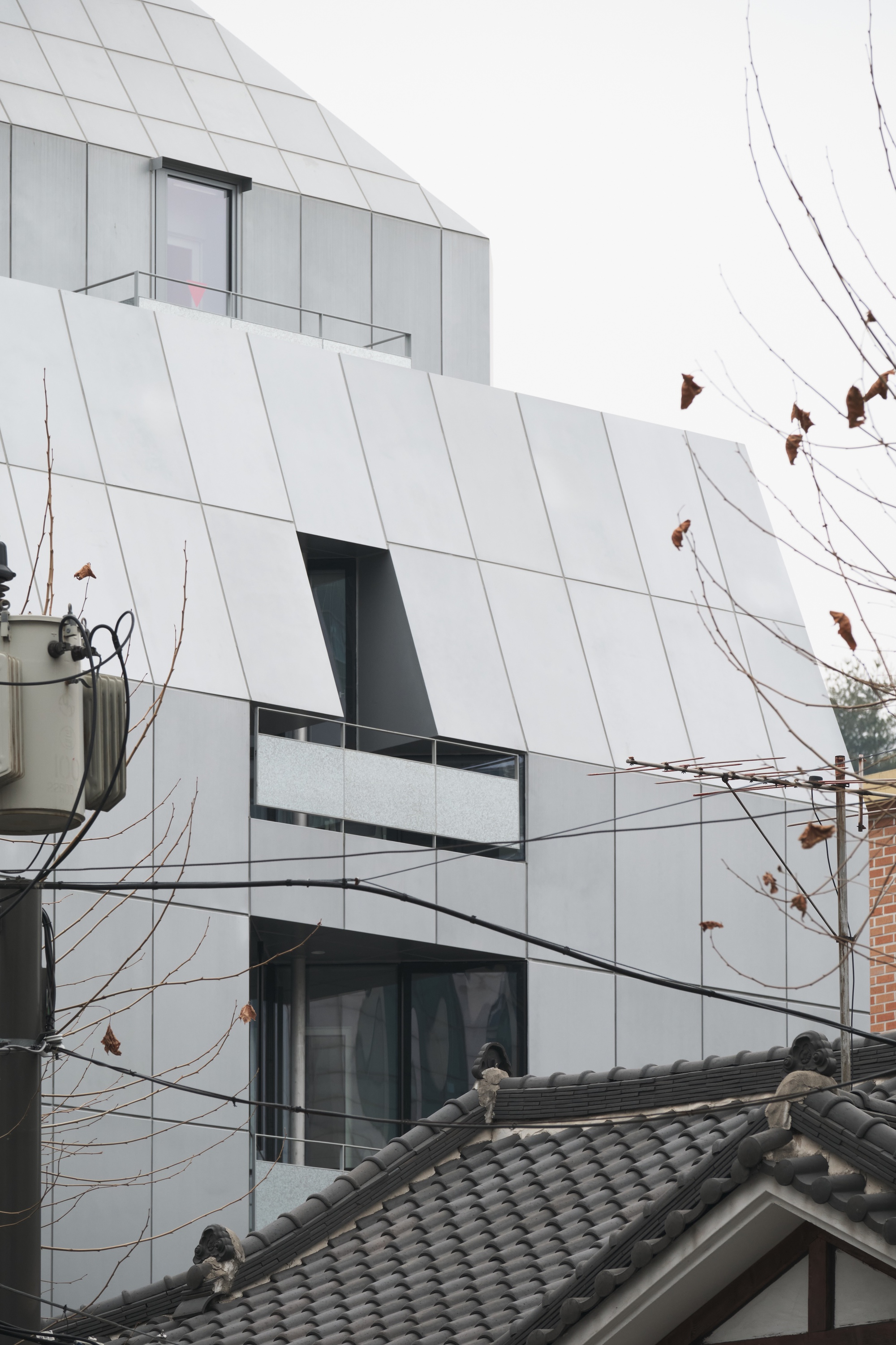 Angled white facade with recessed balconies behind bare tree branches and overhead wires