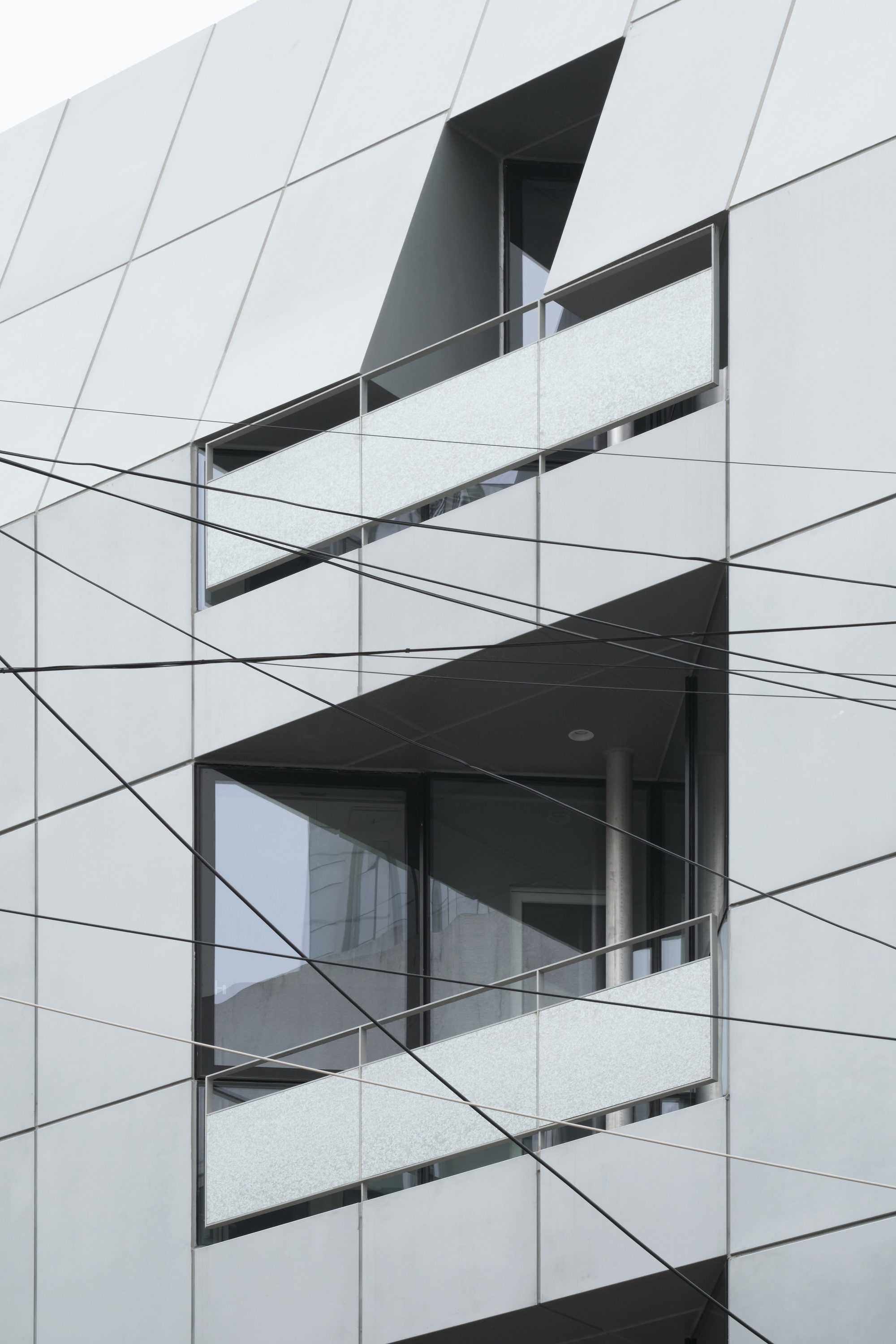 Close-up of stacked balconies with white speckled railings cutting through diagonal panel cladding and utility wires