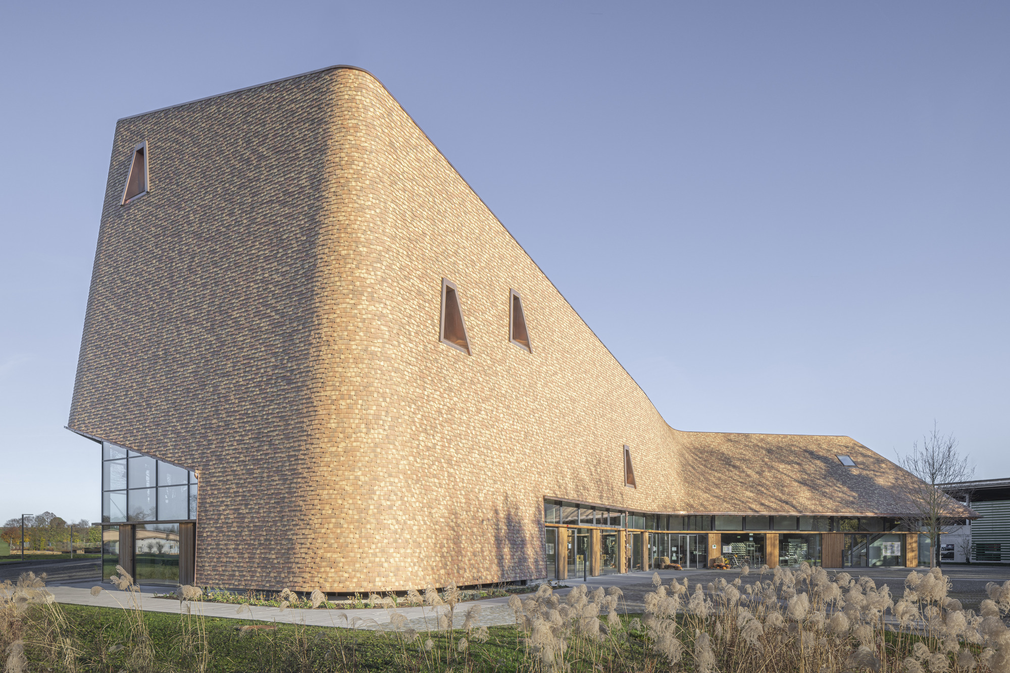 Corner detail of the faceted brick volume with tapered window openings and ornamental grasses