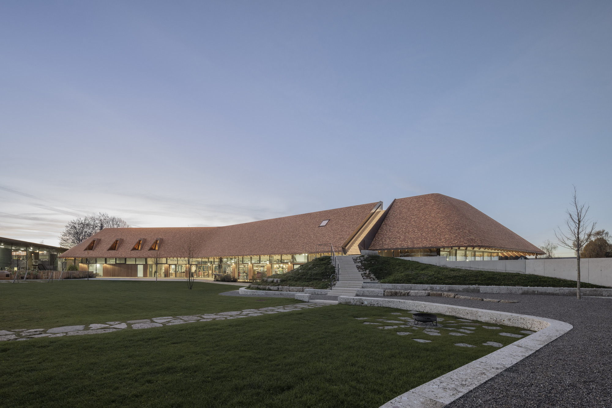 Low-angled view of the undulating shingled roof volumes across a lawn at dusk