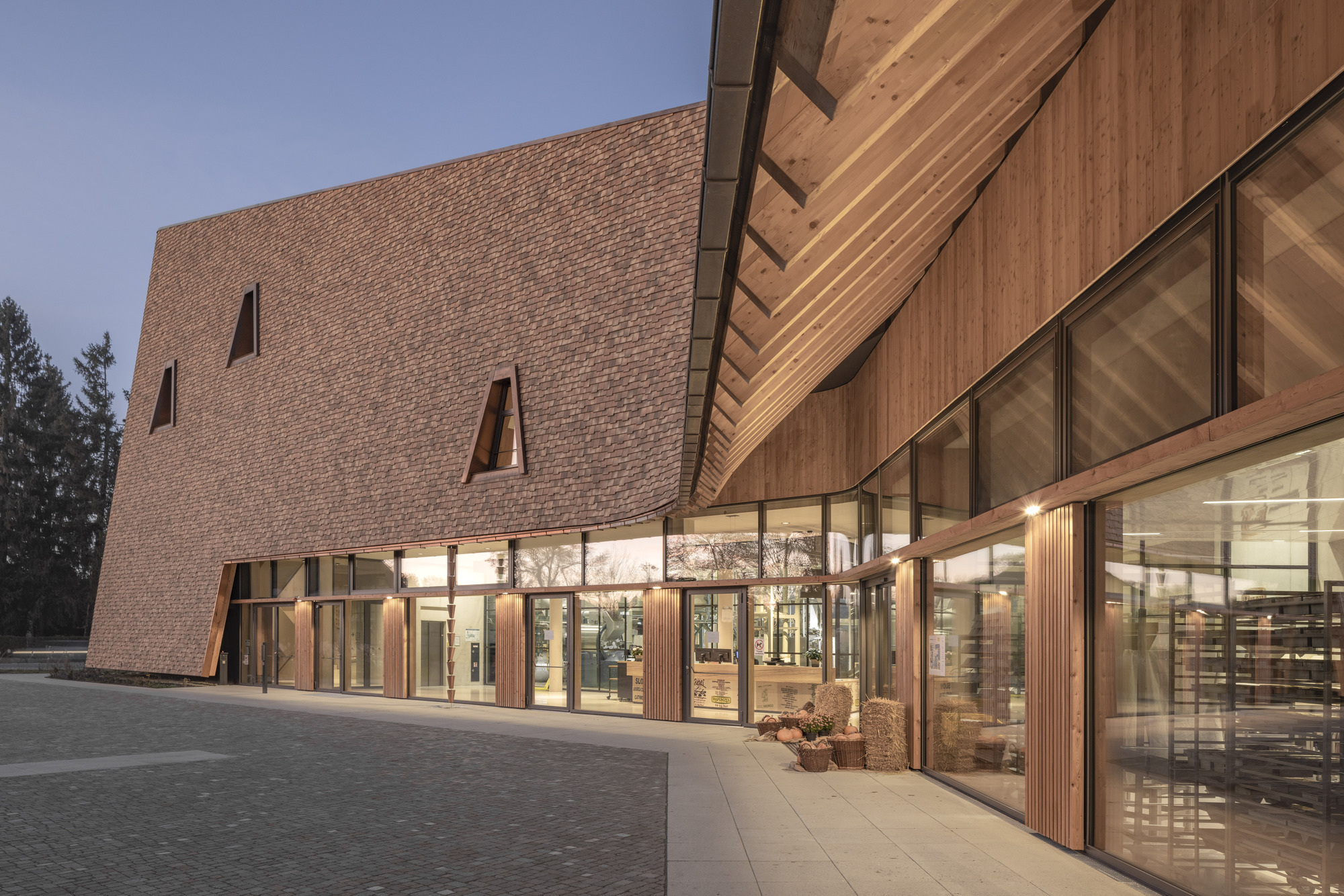 Glass entrance with timber cladding at dusk beneath the overhanging textured brick volume