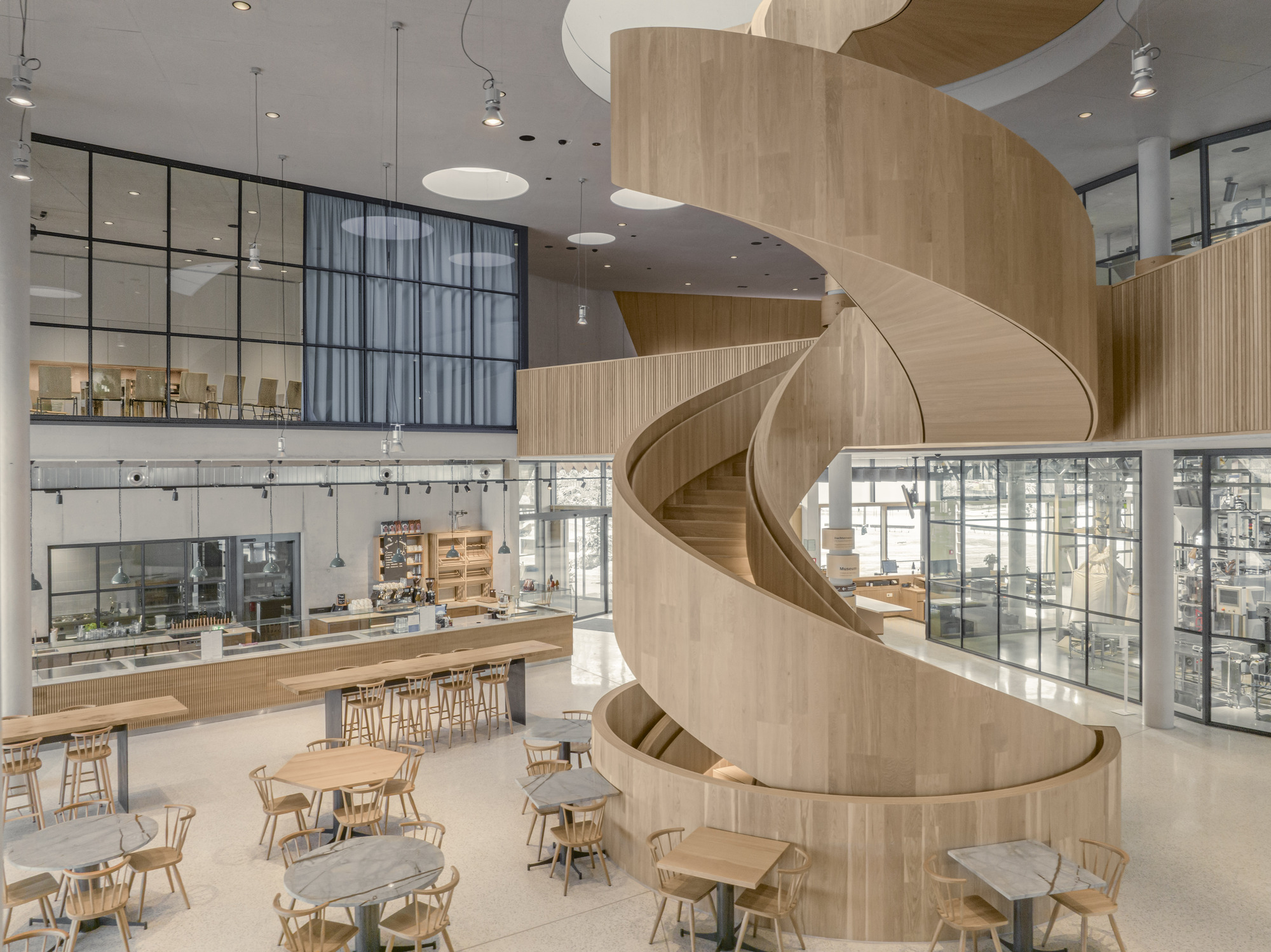 Double-height interior with spiral timber stair and cafe seating area below glazed openings
