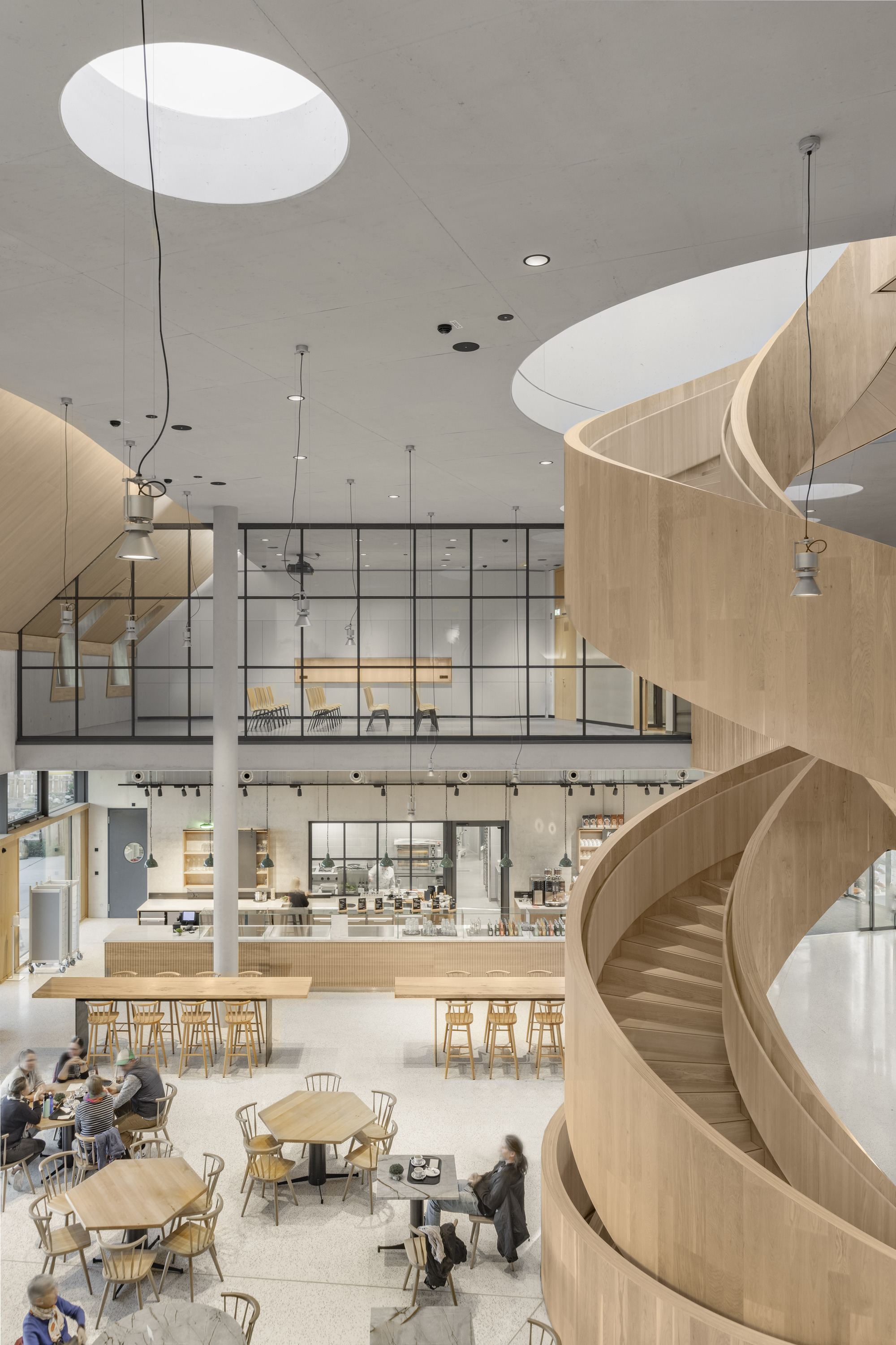 Helical timber staircase viewed from below with patrons seated at tables in the cafe