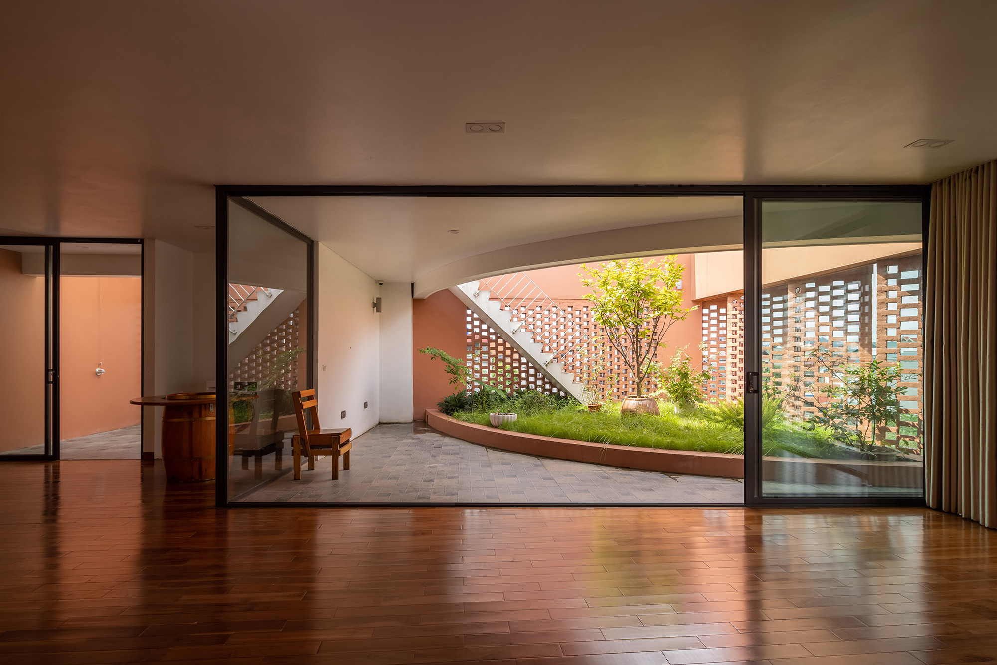 Interior room with timber flooring opening through sliding glass doors to a planted courtyard with perforated walls