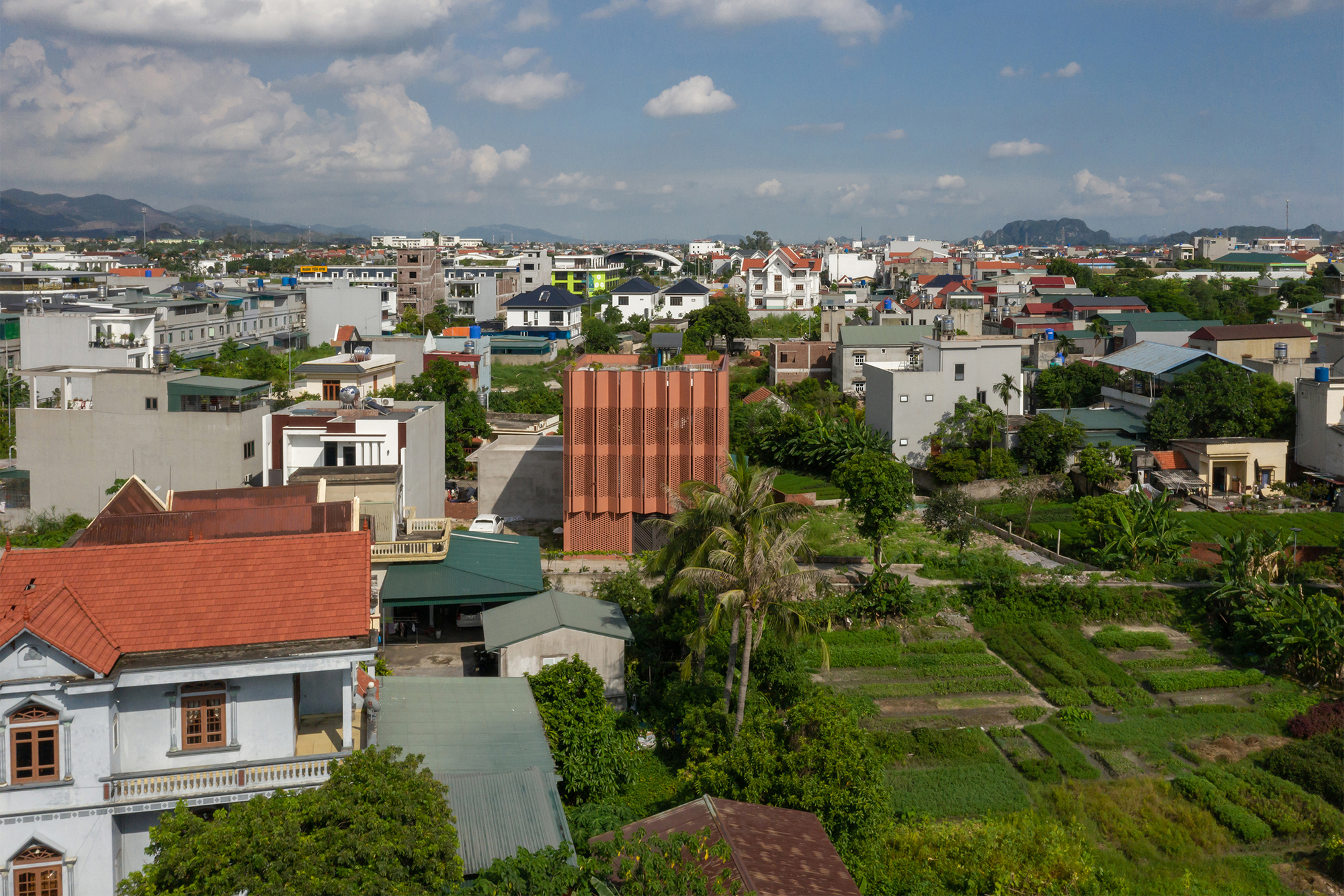 Aerial view of the terracotta tower standing among low-rise residential buildings and garden plots in late afternoon
