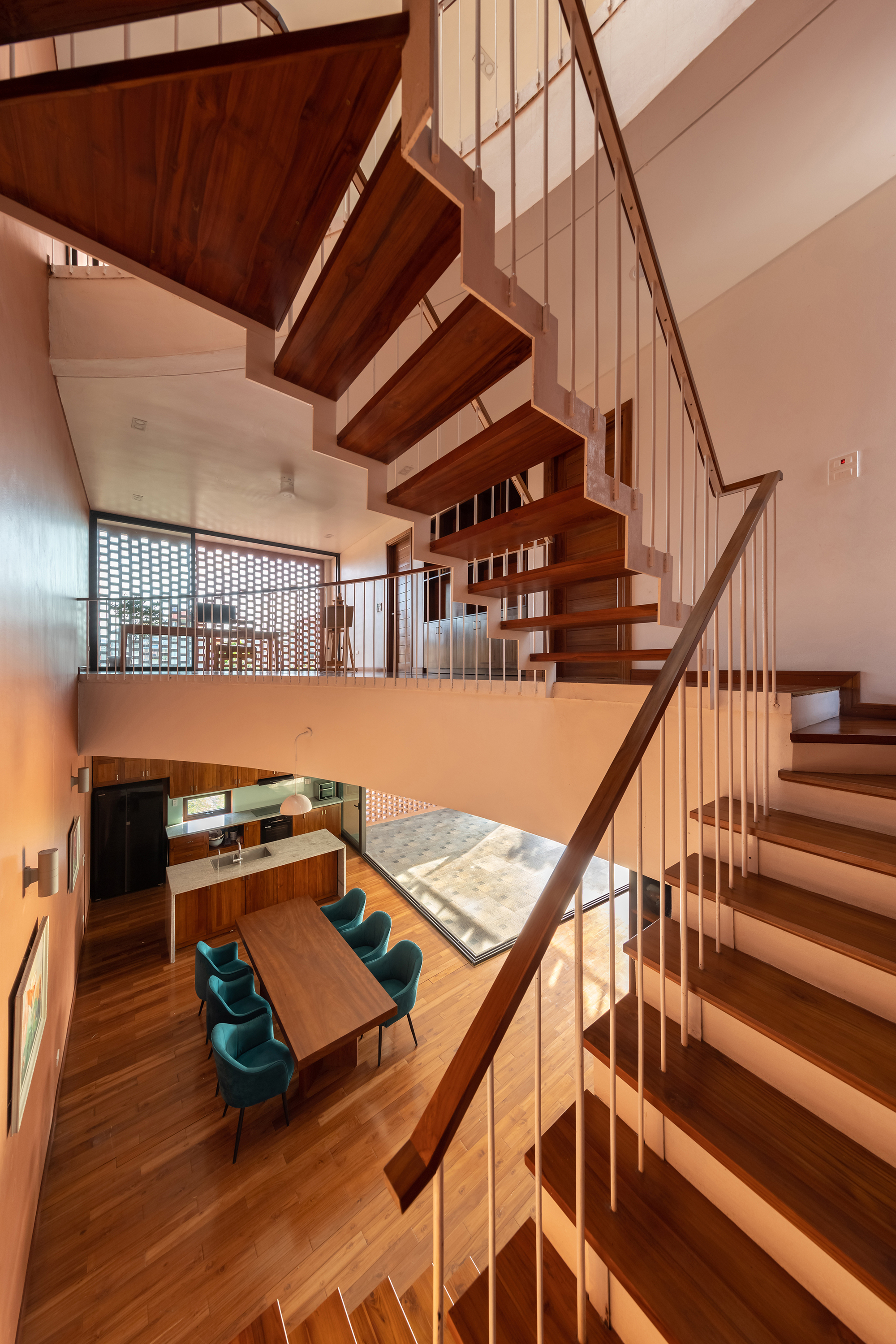 Floating timber staircase with vertical rod railing overlooking a dining area with teal chairs below
