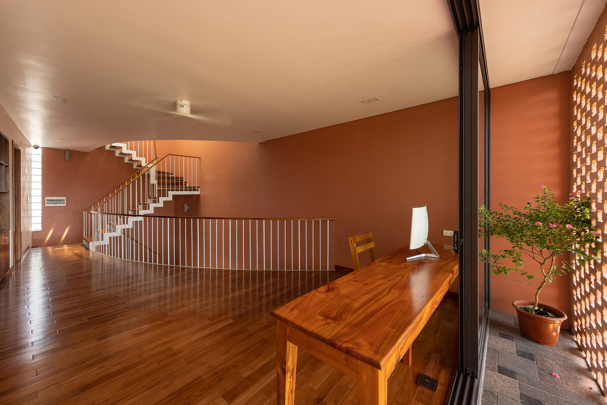 Upper floor corridor with timber desk beside a perforated screen wall and potted bonsai tree