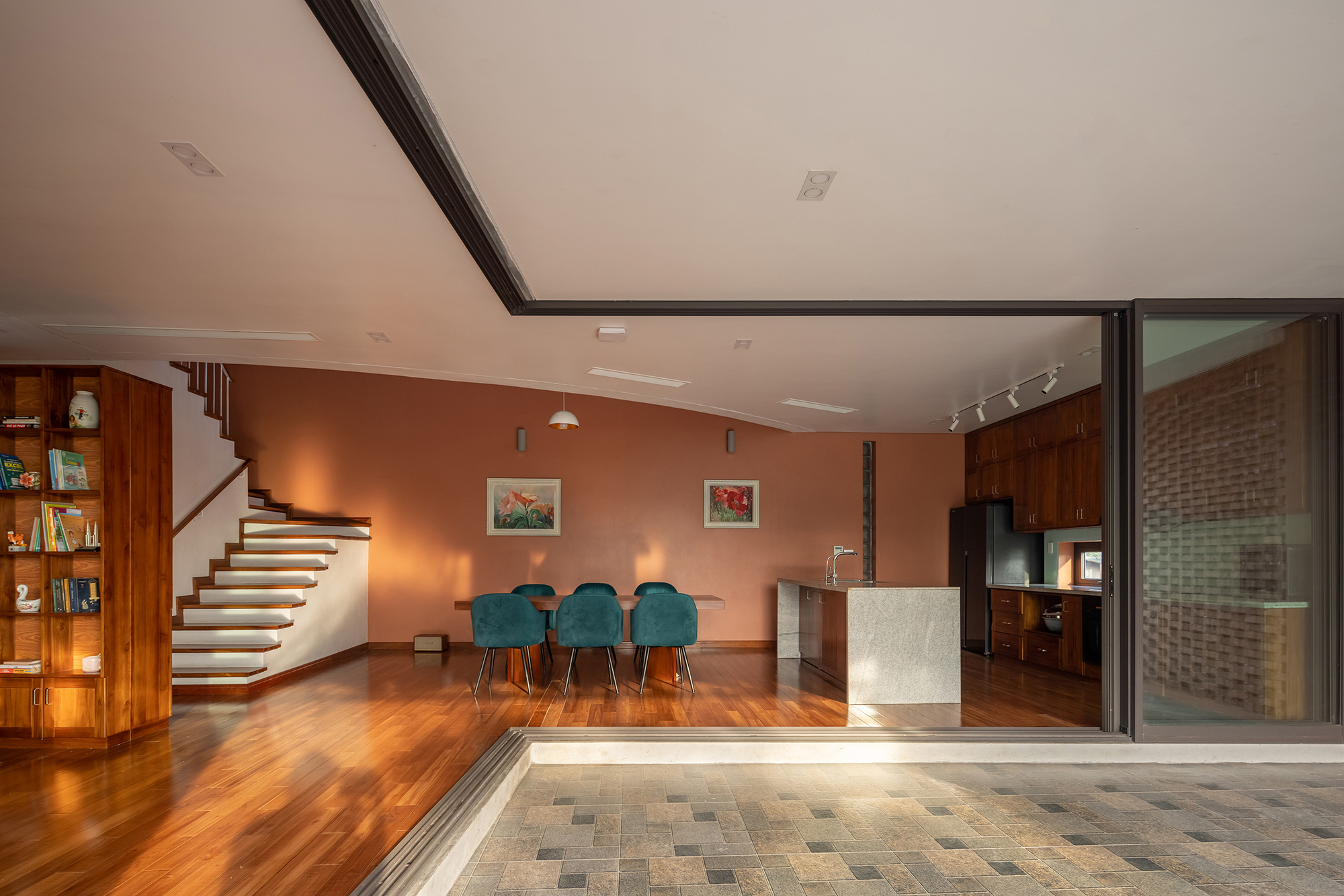 Living space opening to paved courtyard through sliding glass doors beside a curved staircase