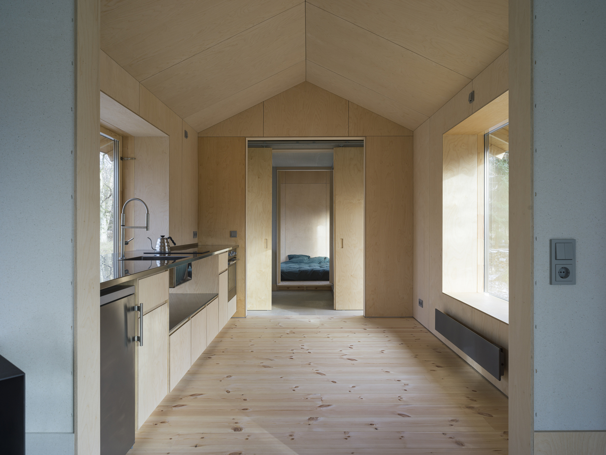 Interior view through the kitchen showing plywood-lined vaulted ceiling and doorway to bedroom beyond