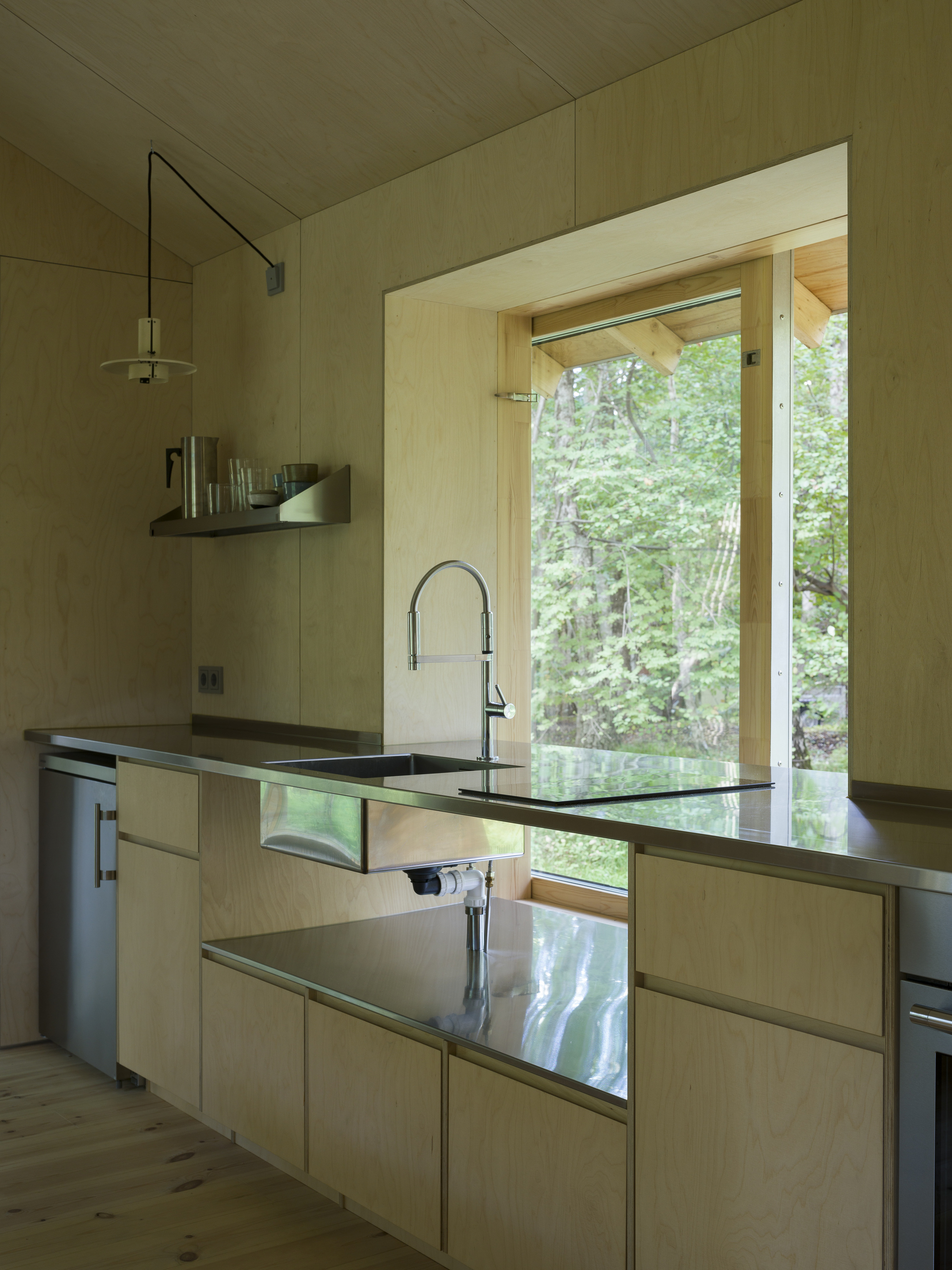 Kitchen with plywood cabinetry, dark countertop, and large window framing summer foliage