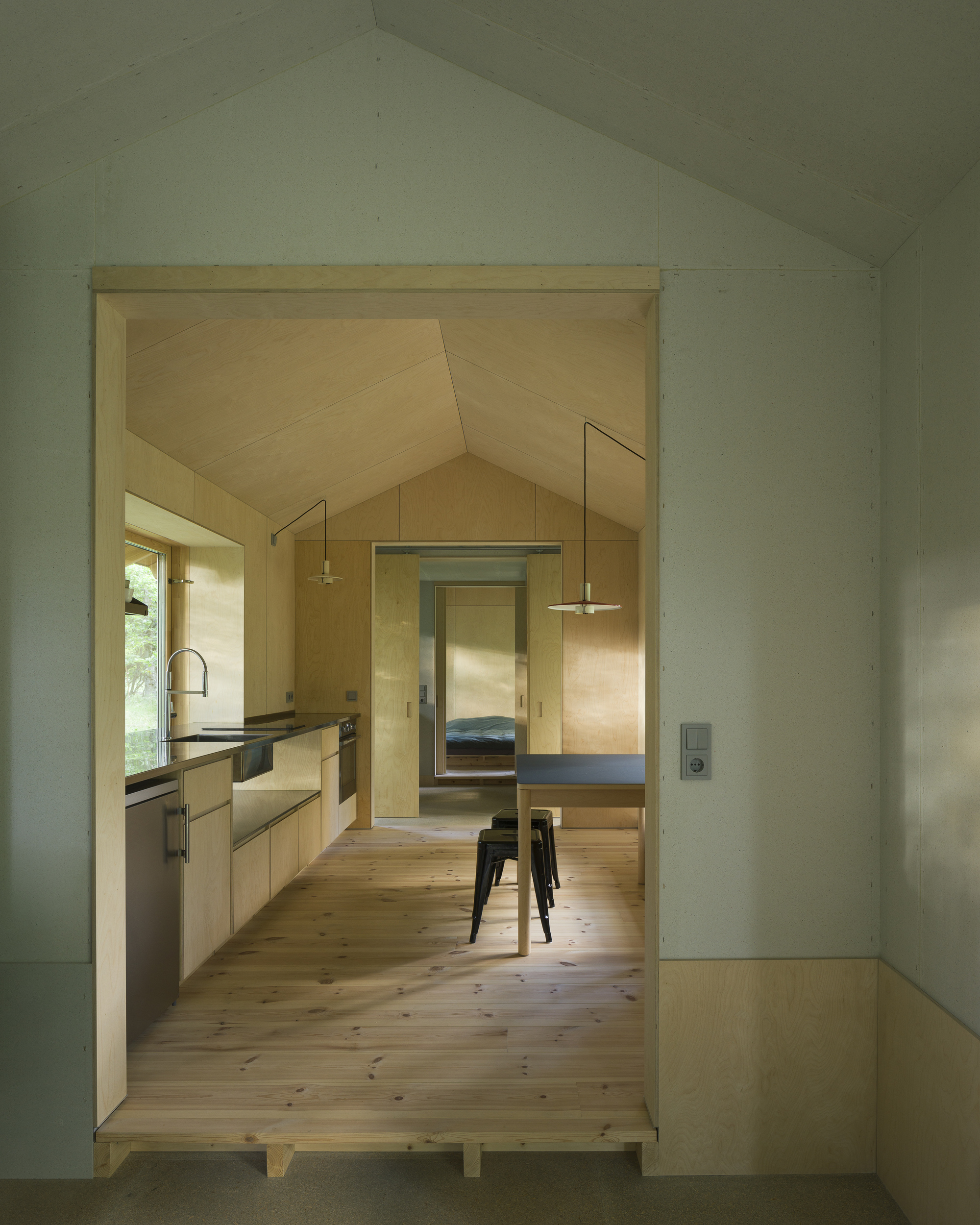 View through a doorway revealing the plywood-lined kitchen and dining space with pendant lights
