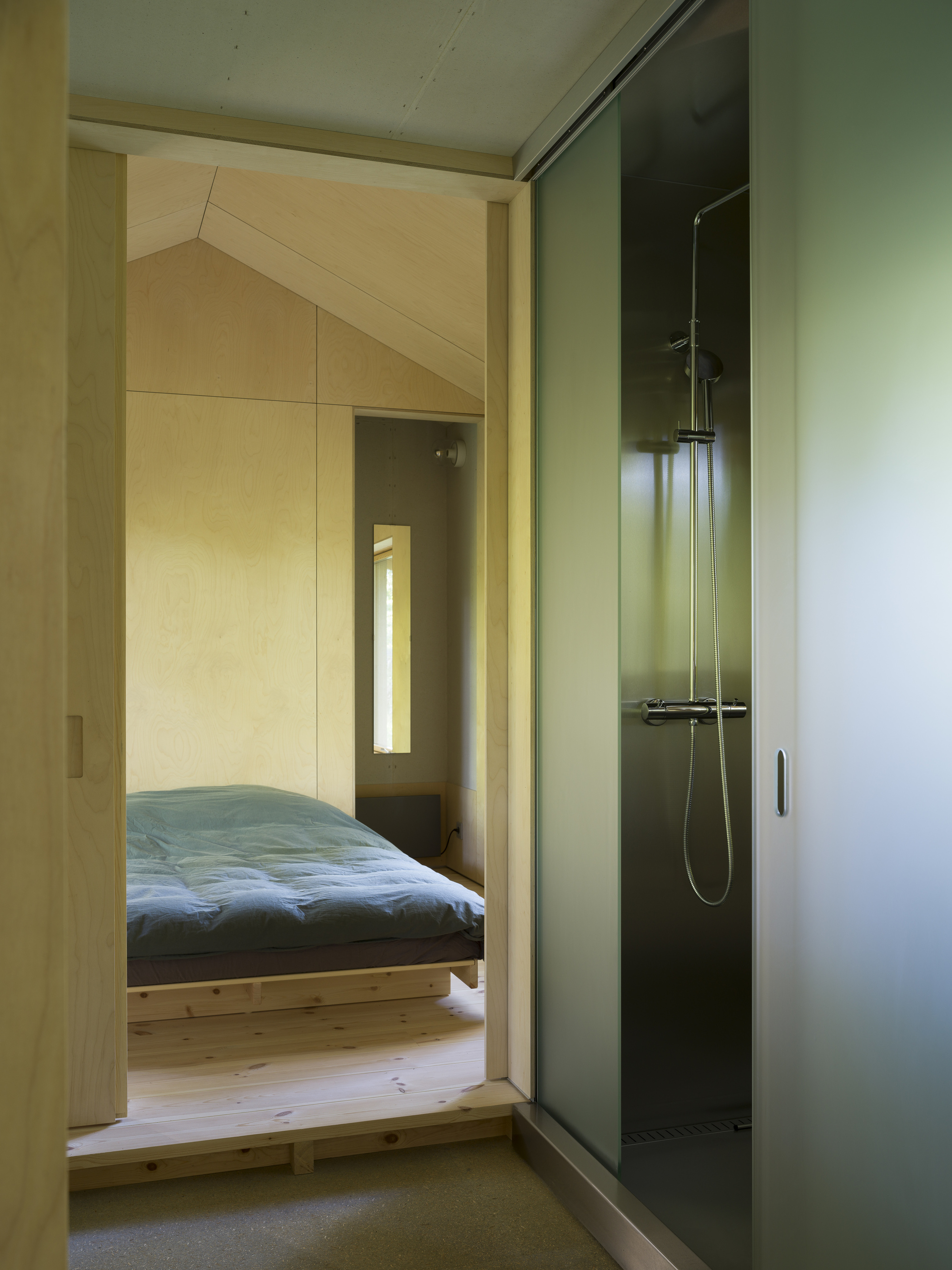 Bathroom with glass shower enclosure and view through doorway to bedroom with blue bedding