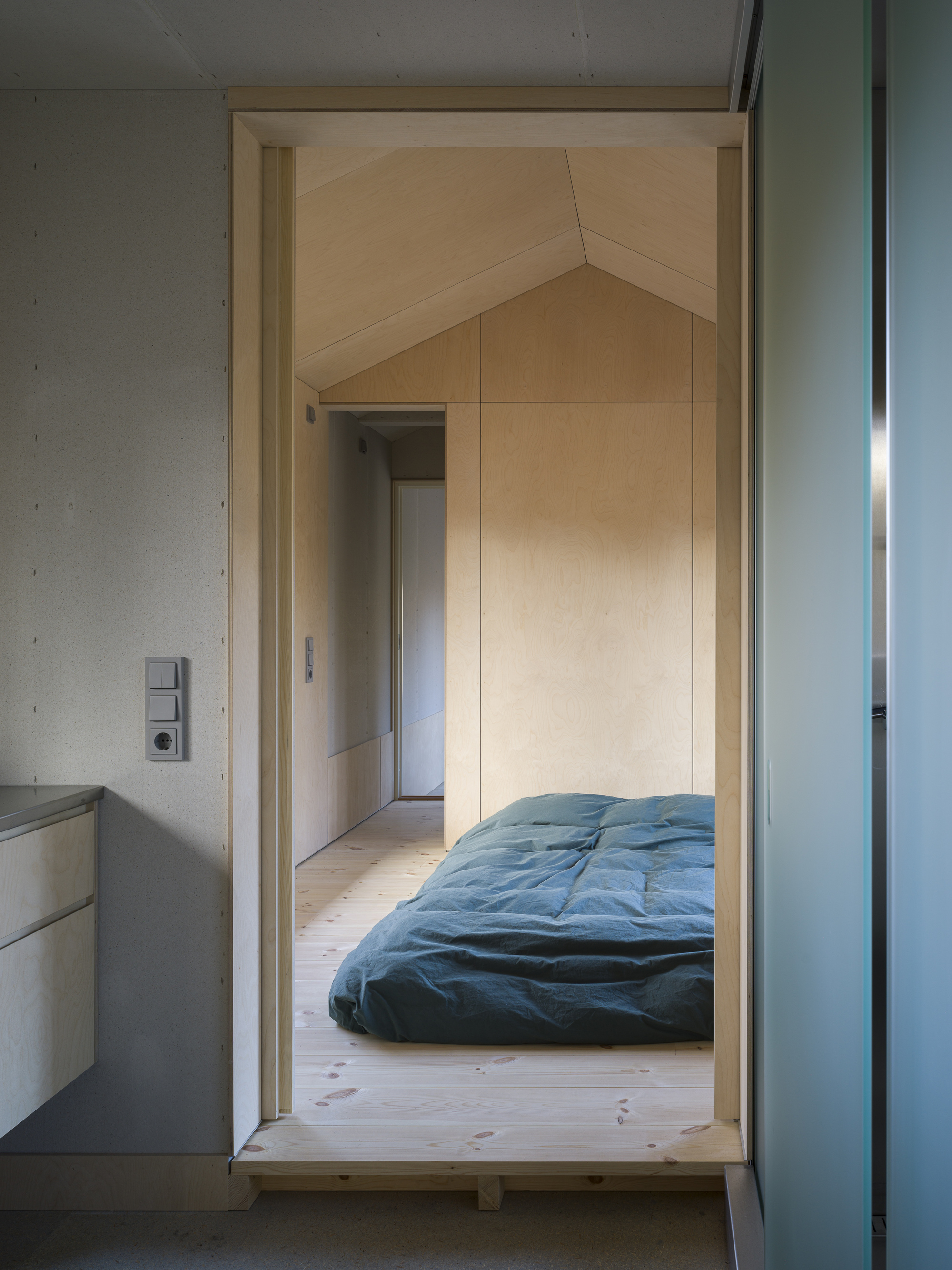 Doorway leading to a raised bedroom platform with plywood lining and a green futon