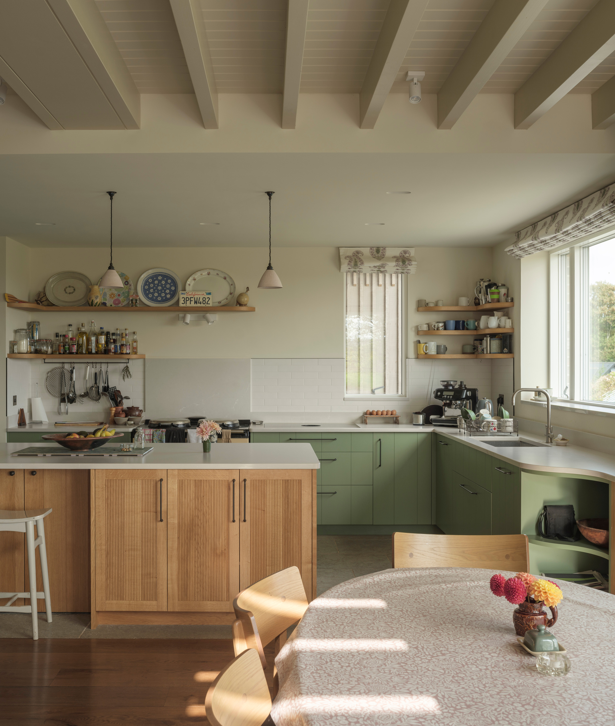 Kitchen with green cabinetry, timber island and exposed ceiling beams in afternoon light