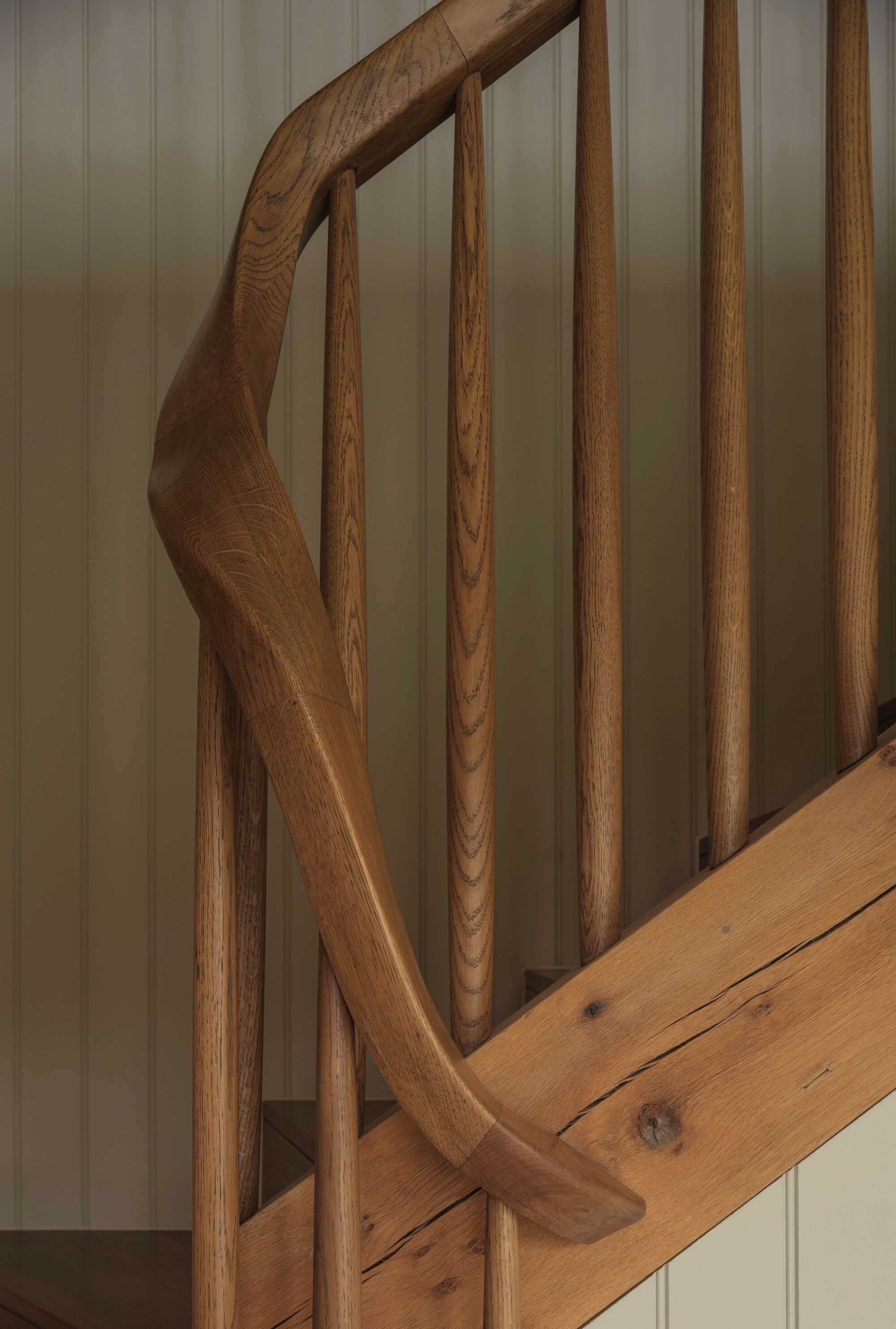 Close-up of curved oak handrail and vertical balusters against painted tongue-and-groove wall panels