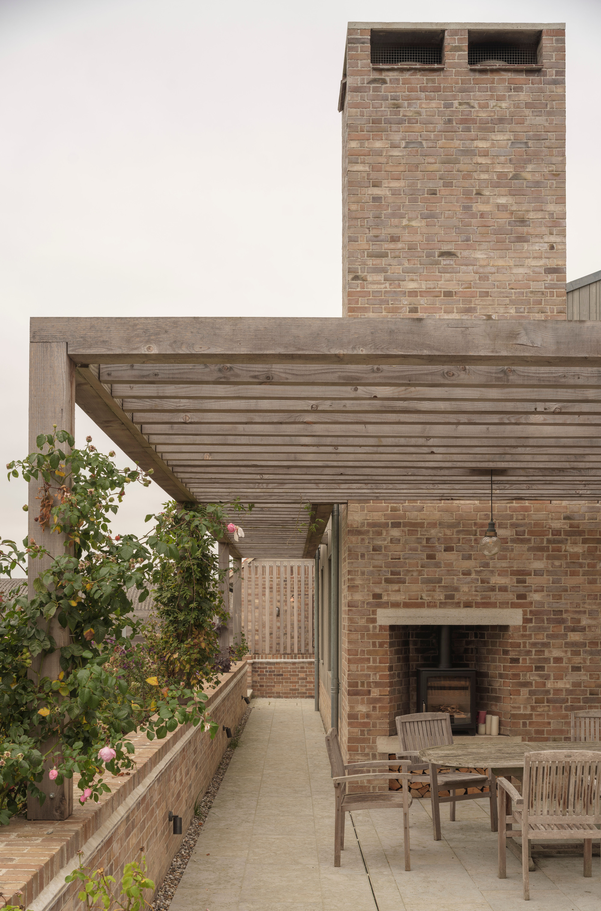 Brick courtyard with timber pergola, planted bed and brick chimney tower under overcast sky