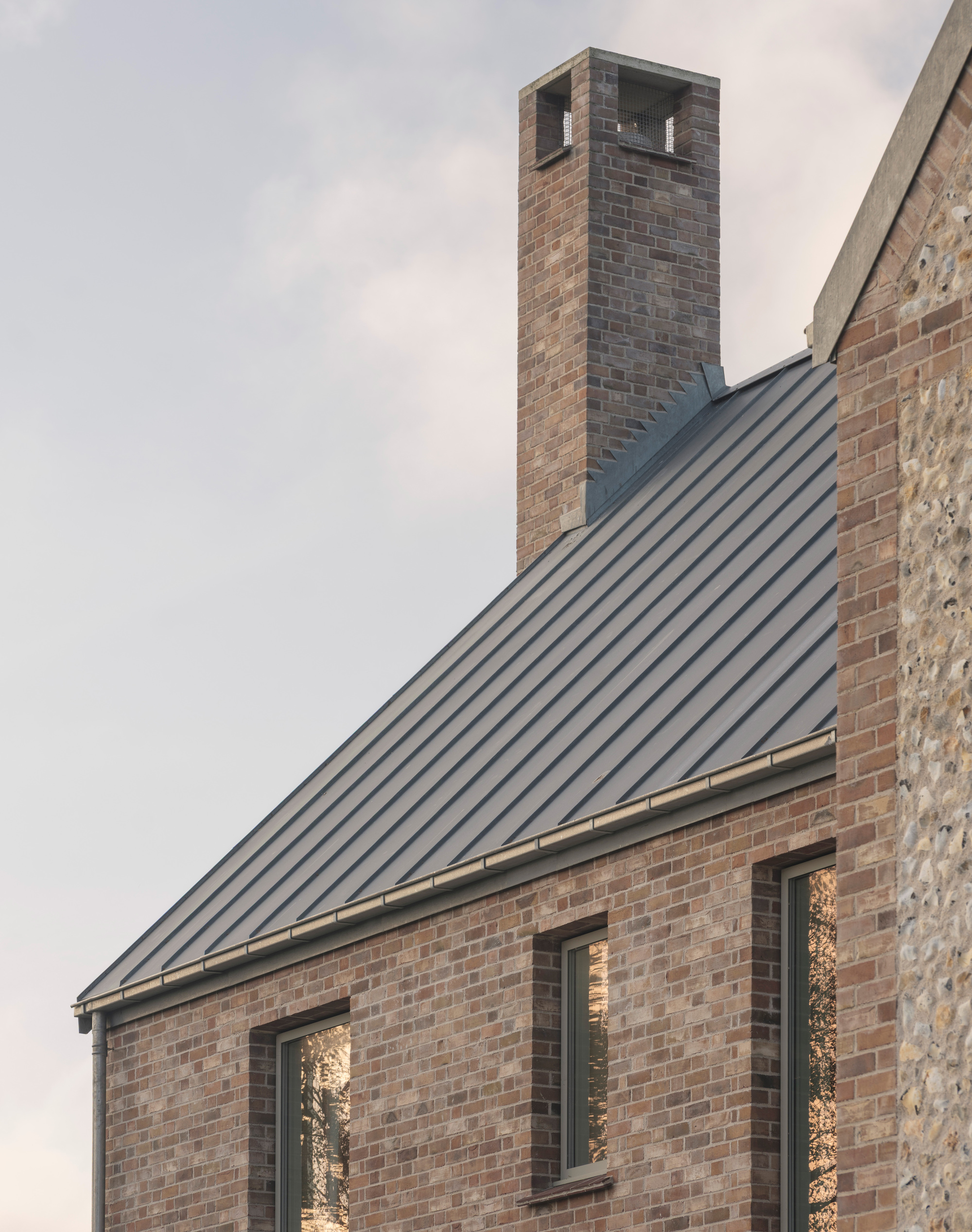 Brick gable with standing seam metal roof and chimney tower at dusk