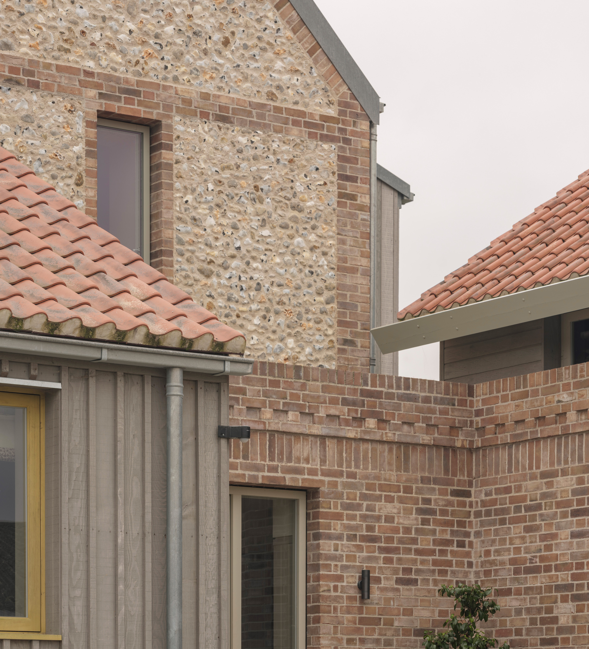 Flint and brick facade detail with clay tile roofs flanking a narrow window