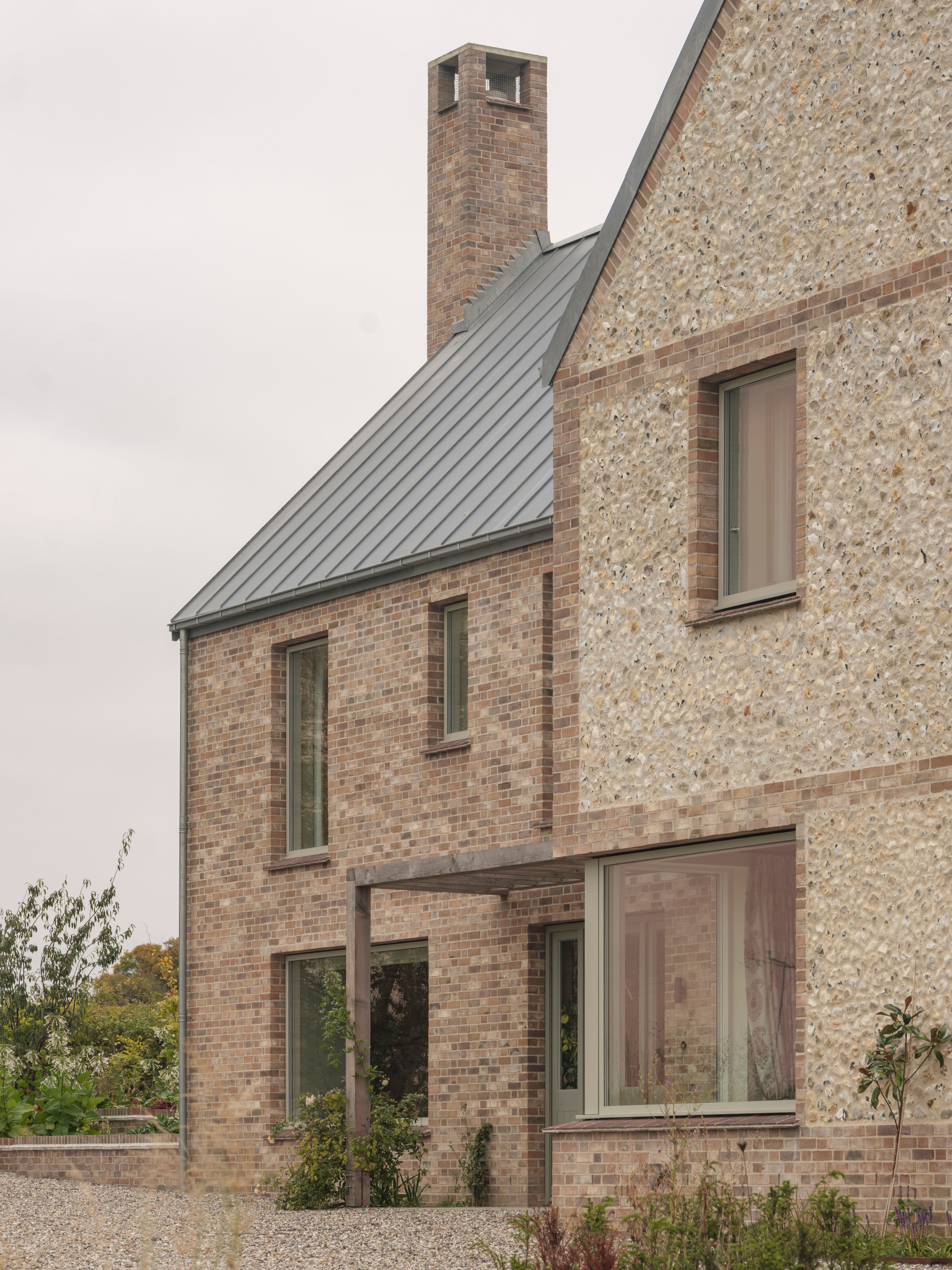 Courtyard view showing brick chimney stack and metal standing seam roof against knapped flint gable wall