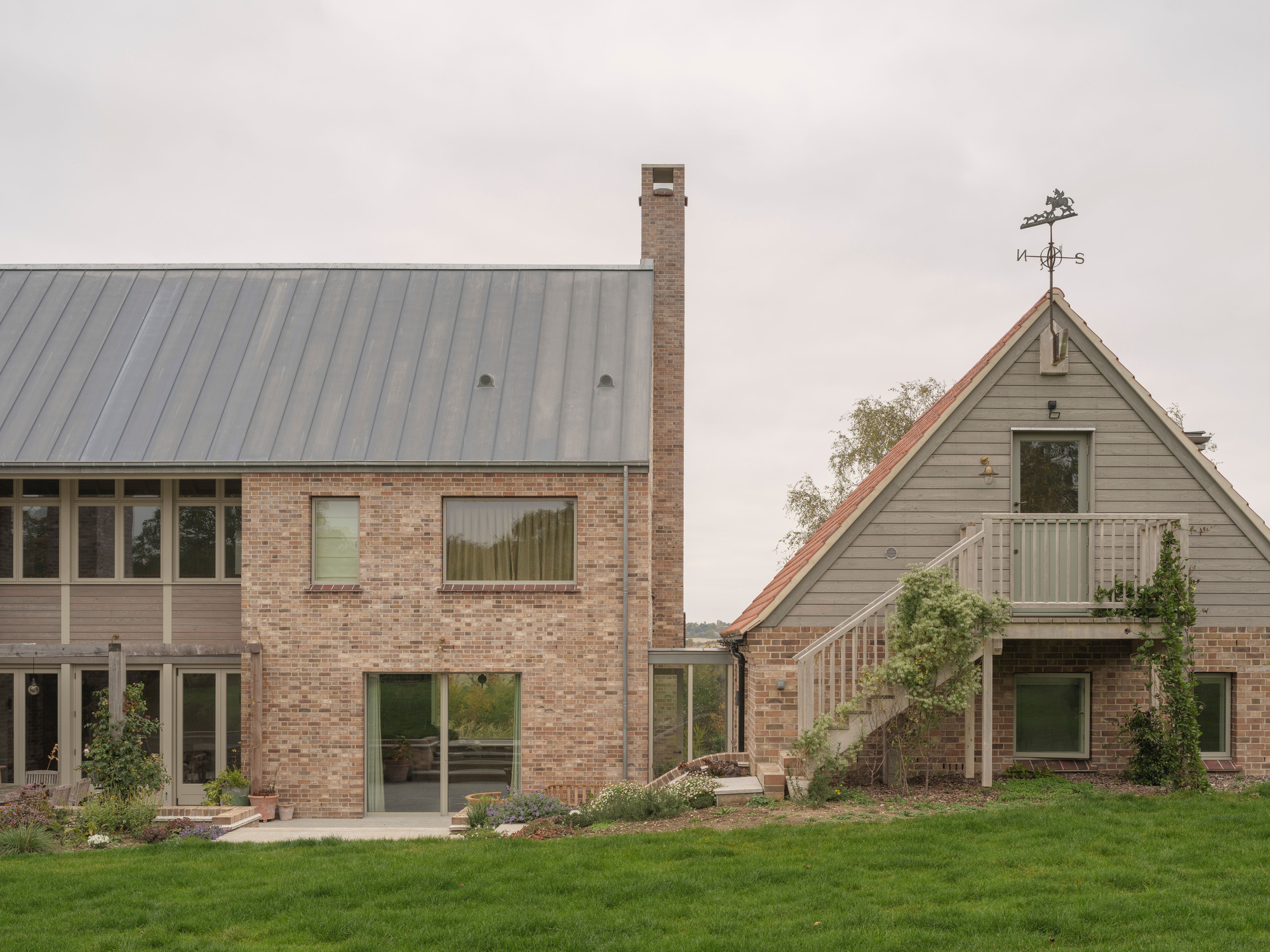 Garden elevation showing metal roof volumes and weather vane atop timber-clad gable with lawn foreground